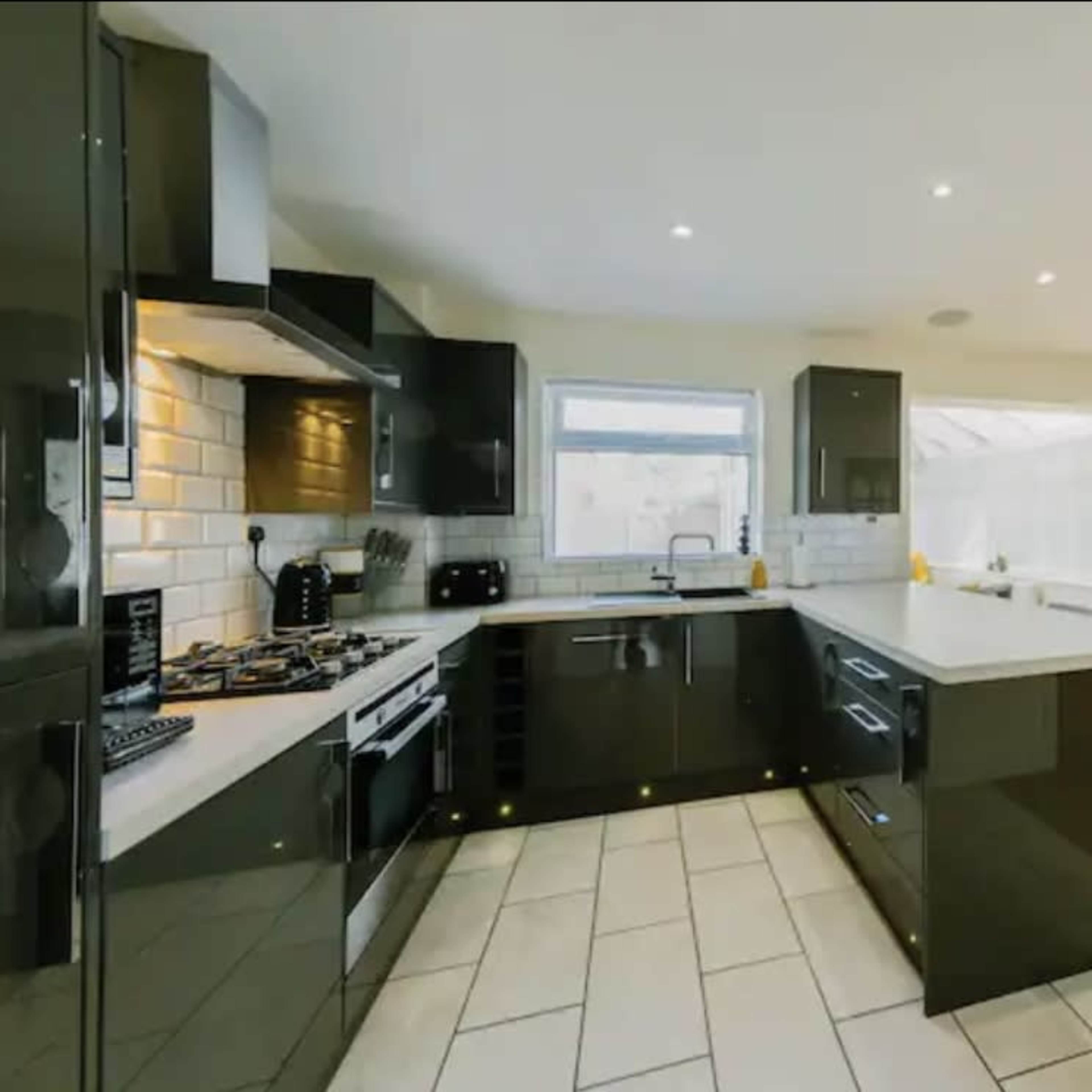 A modern kitchen featuring black cabinetry, white countertops, and an adjoining dining area with a wooden floor.