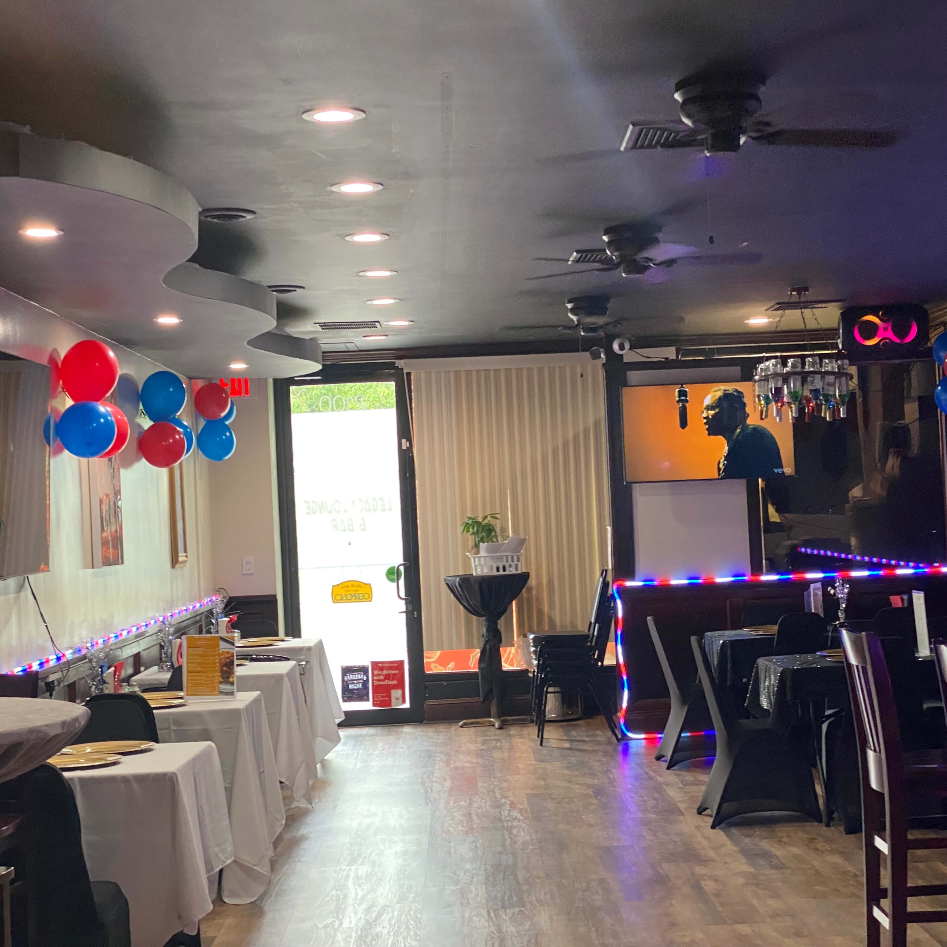 The interior of a restaurant features tables covered with white tablecloths, decorations in red and blue, and a stage area illuminated by soft lighting.