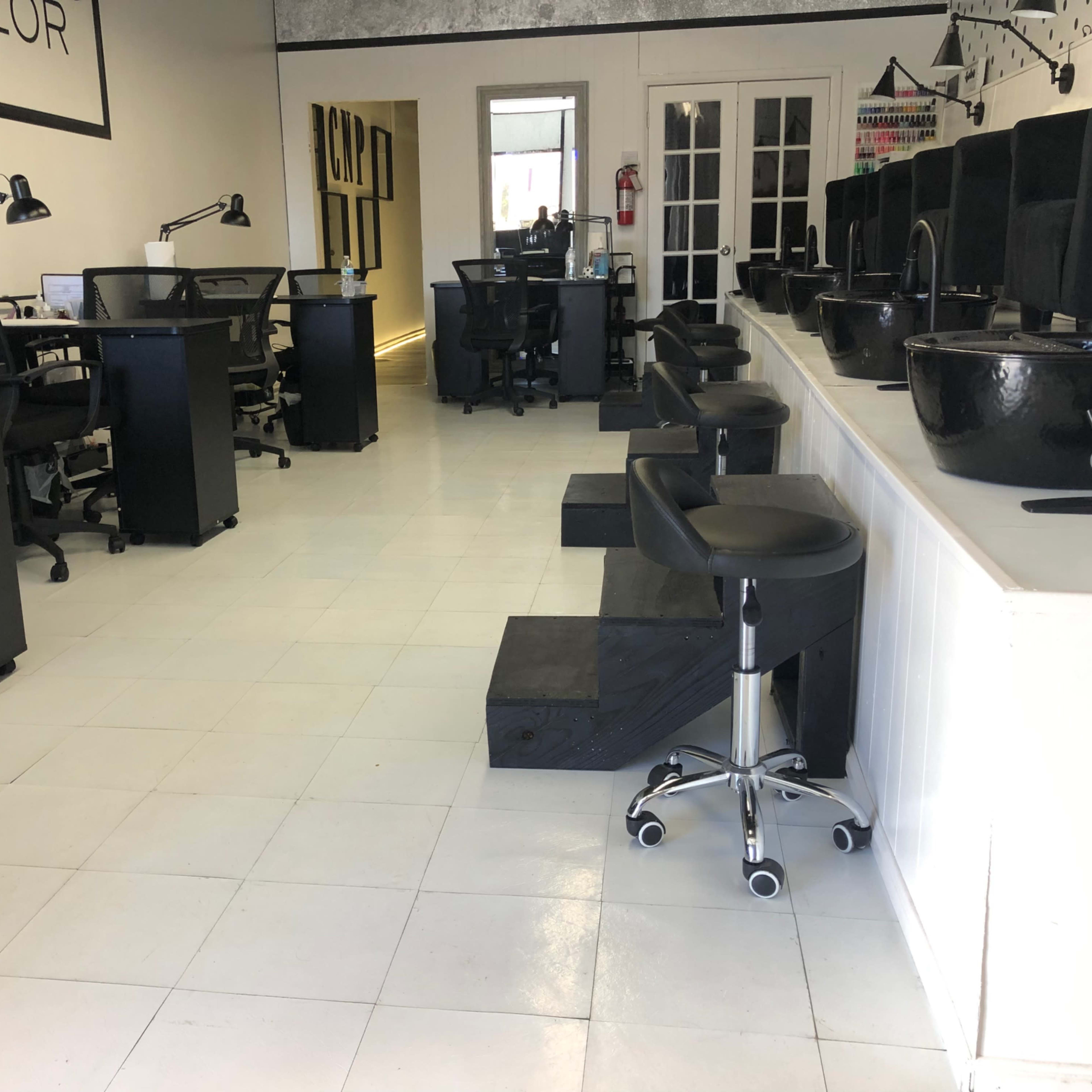 The interior of a nail salon with several workstations, black pedicure bowls, and modern chairs arranged in a spacious layout.