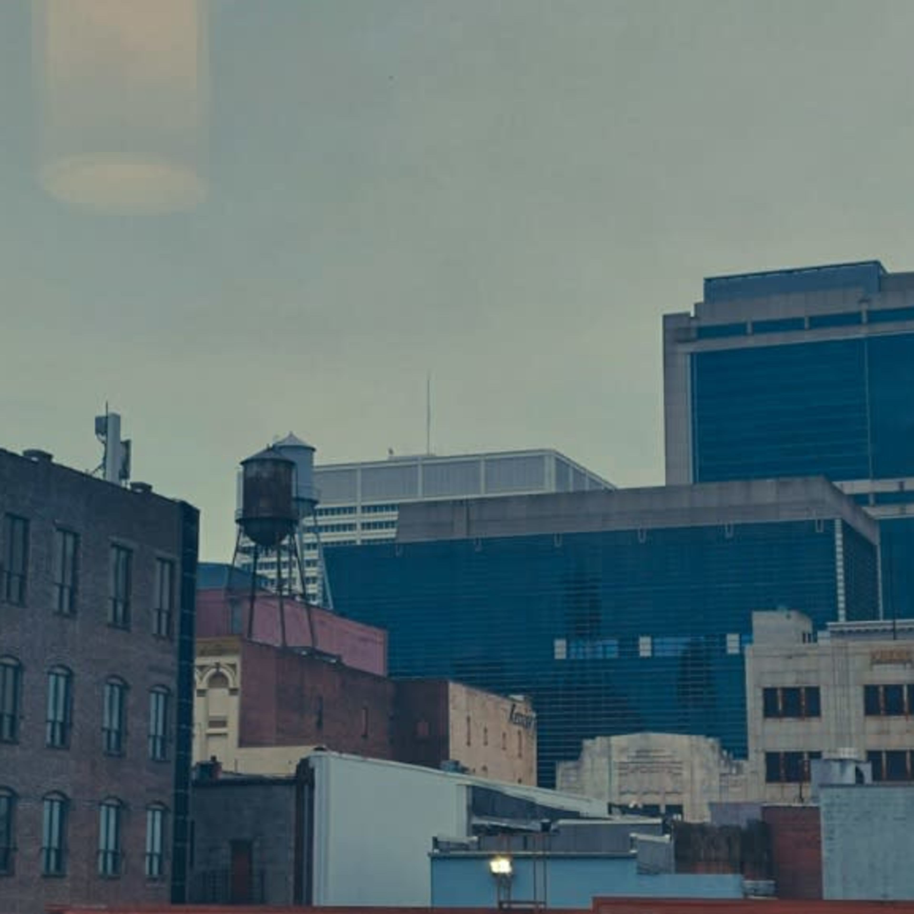 A cityscape featuring a mix of older brick buildings and modern glass structures, with a water tower prominently situated on a rooftop.