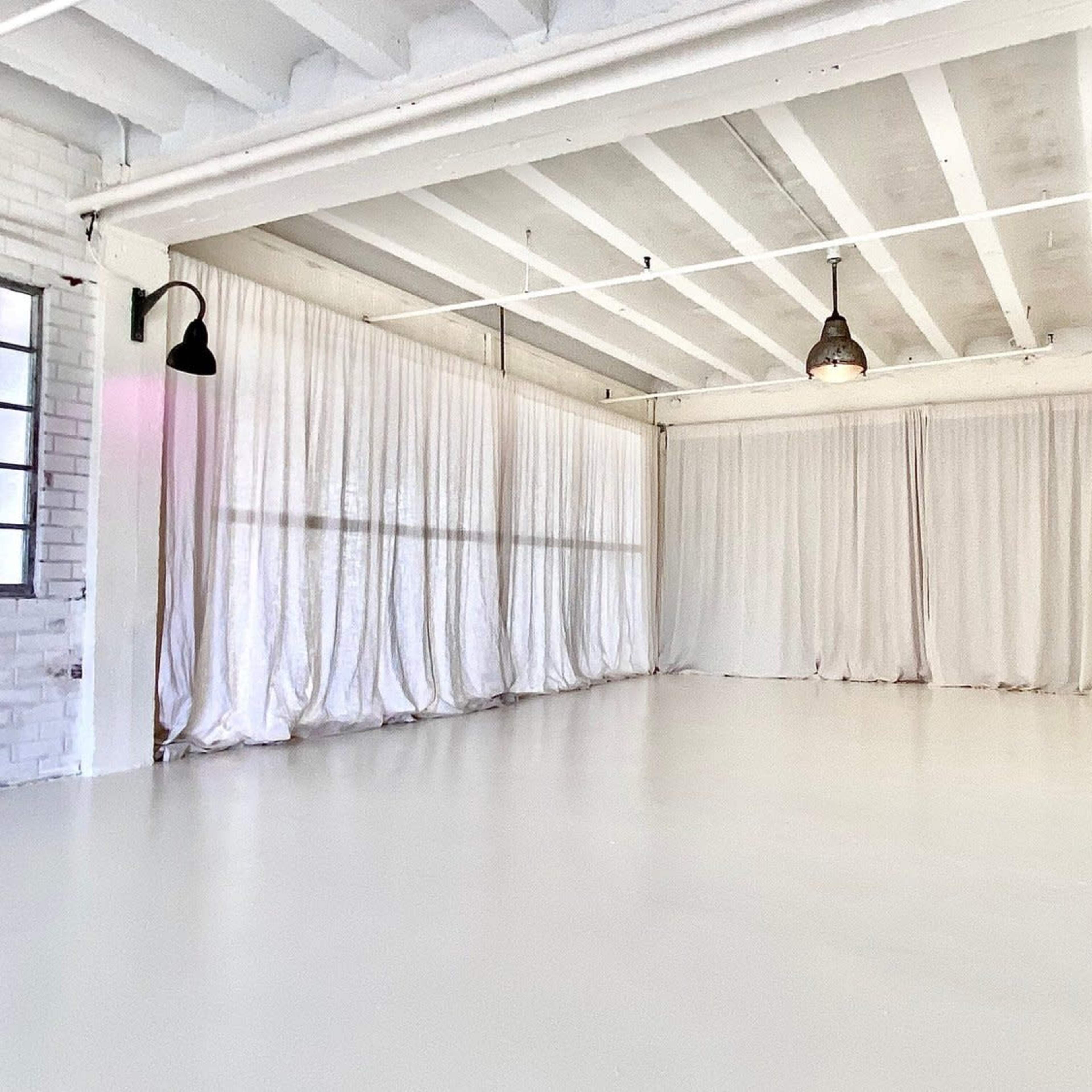 A spacious room with white walls, a polished floor, and large curtains covering the windows.