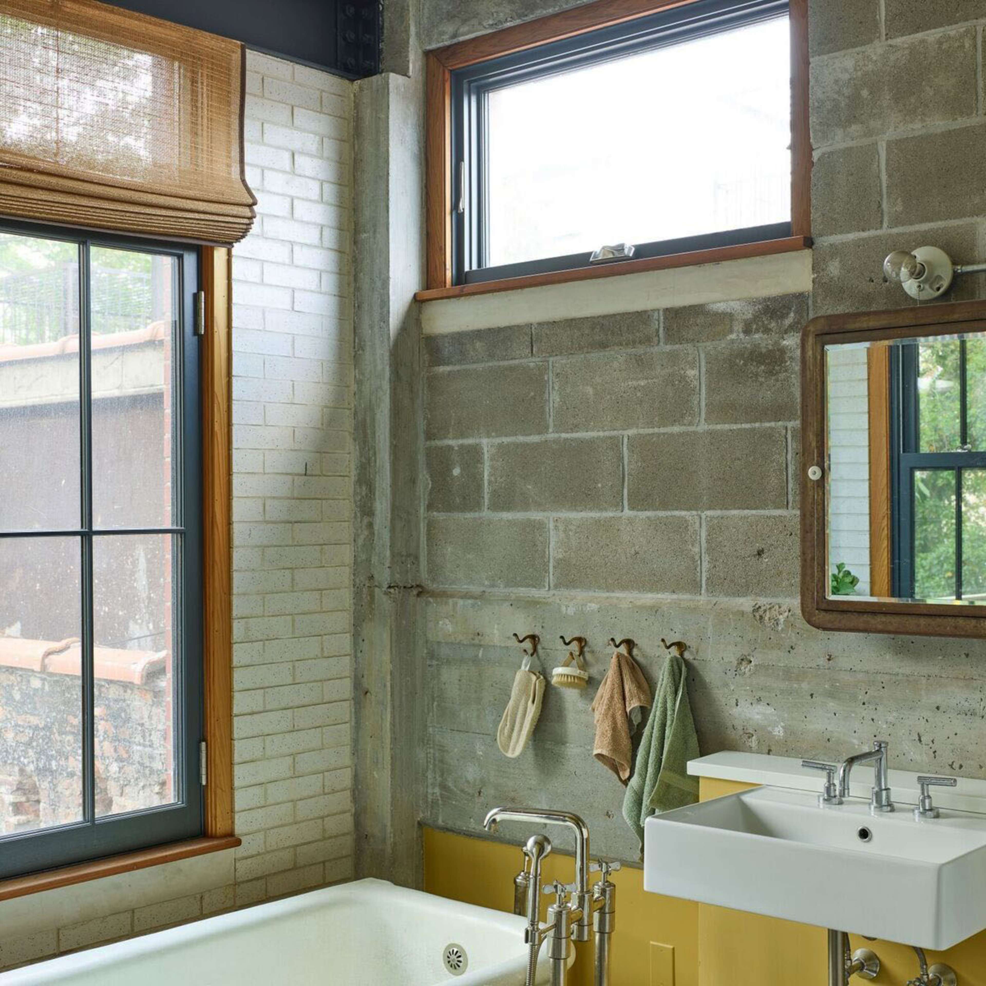 A modern bathroom with a freestanding bathtub, a wall-mounted sink, and a patterned tile floor, illuminated by natural light from large windows.