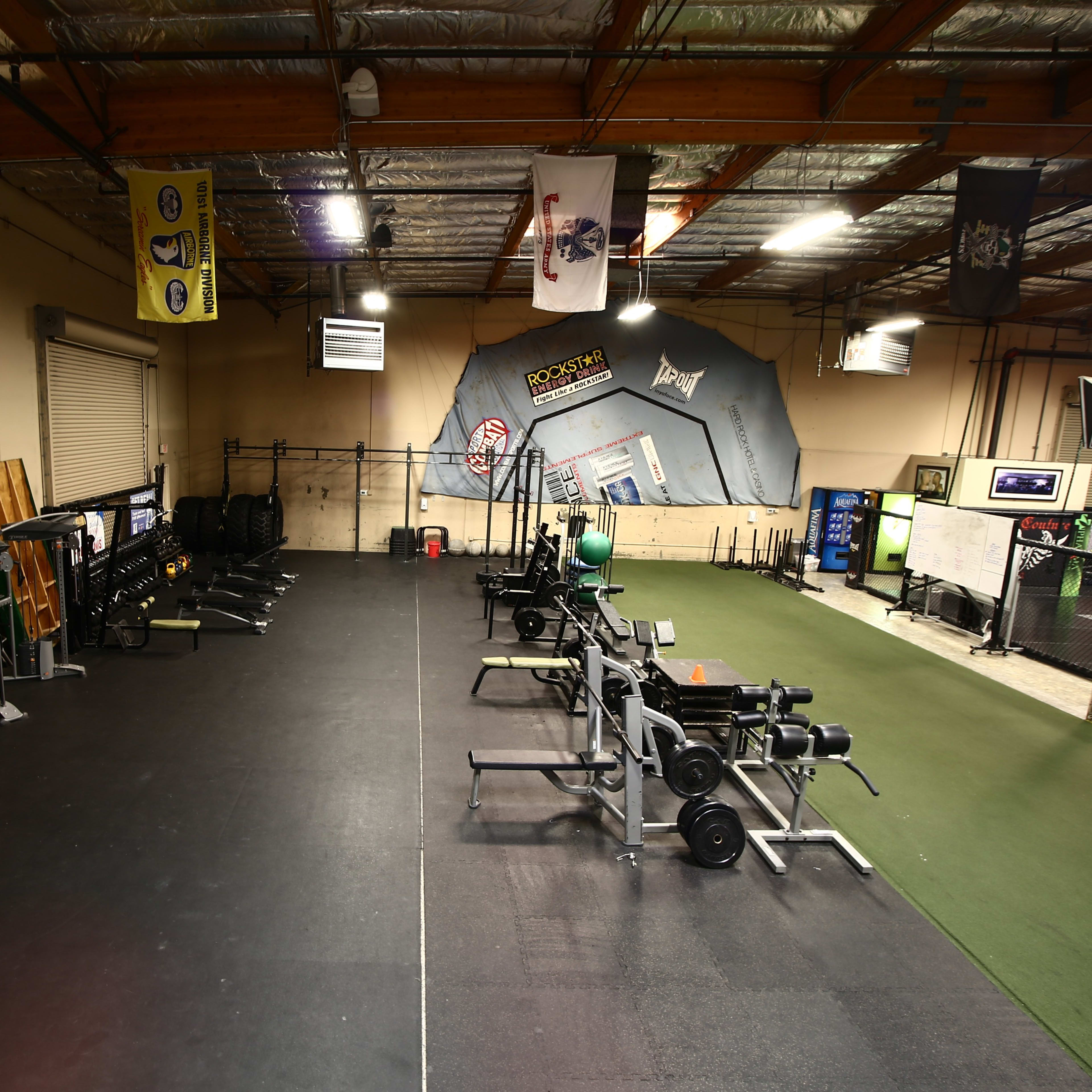 A spacious gym with various weightlifting equipment and exercise areas, separated by a black rubber floor and green turf.