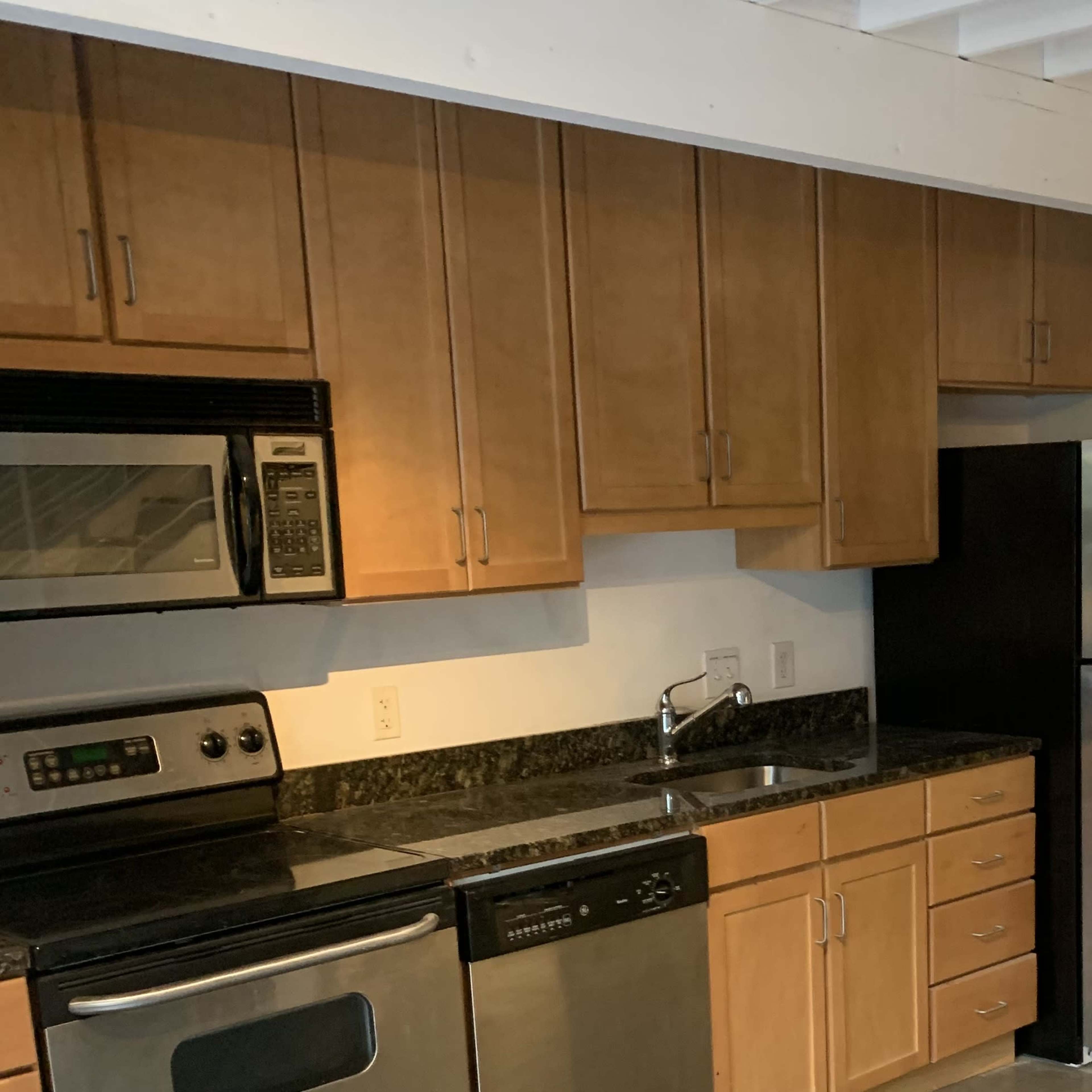 A kitchen with wooden cabinets, stainless steel appliances, and black granite countertops.