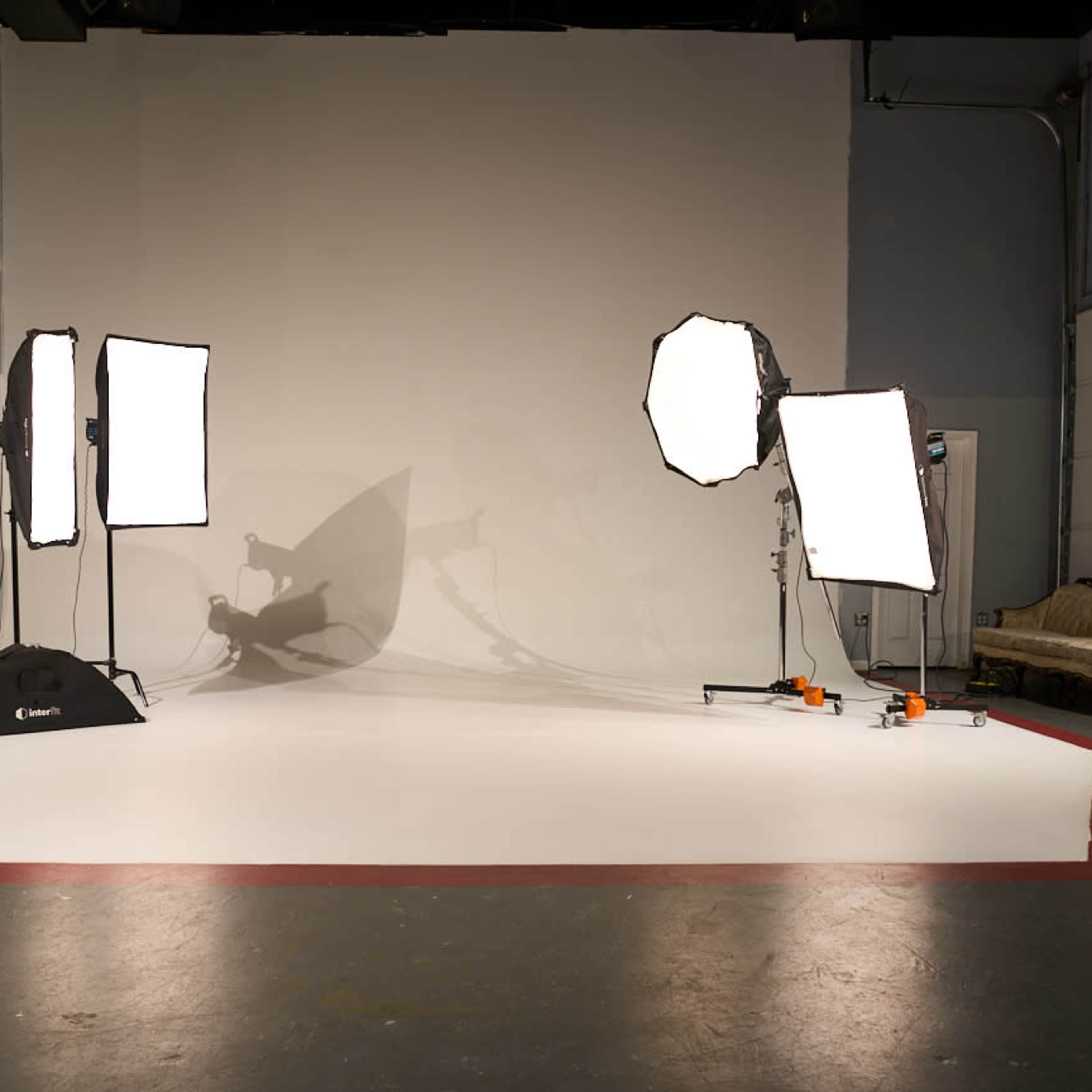 A photography studio with three softbox lights positioned around a blank backdrop and a white floor.
