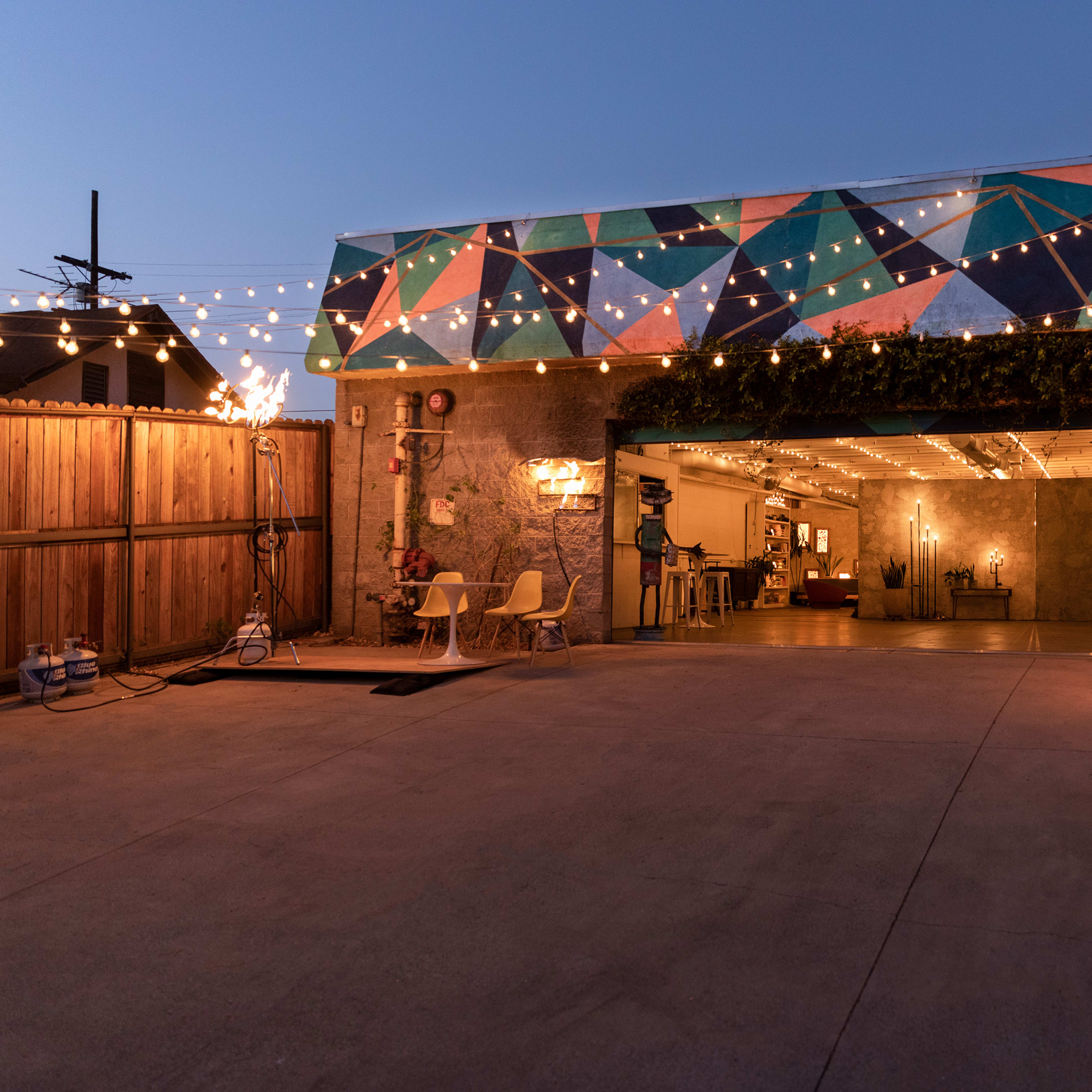 A garage with a colorful geometric mural, string lights overhead, and a spacious driveway leading to an open door.