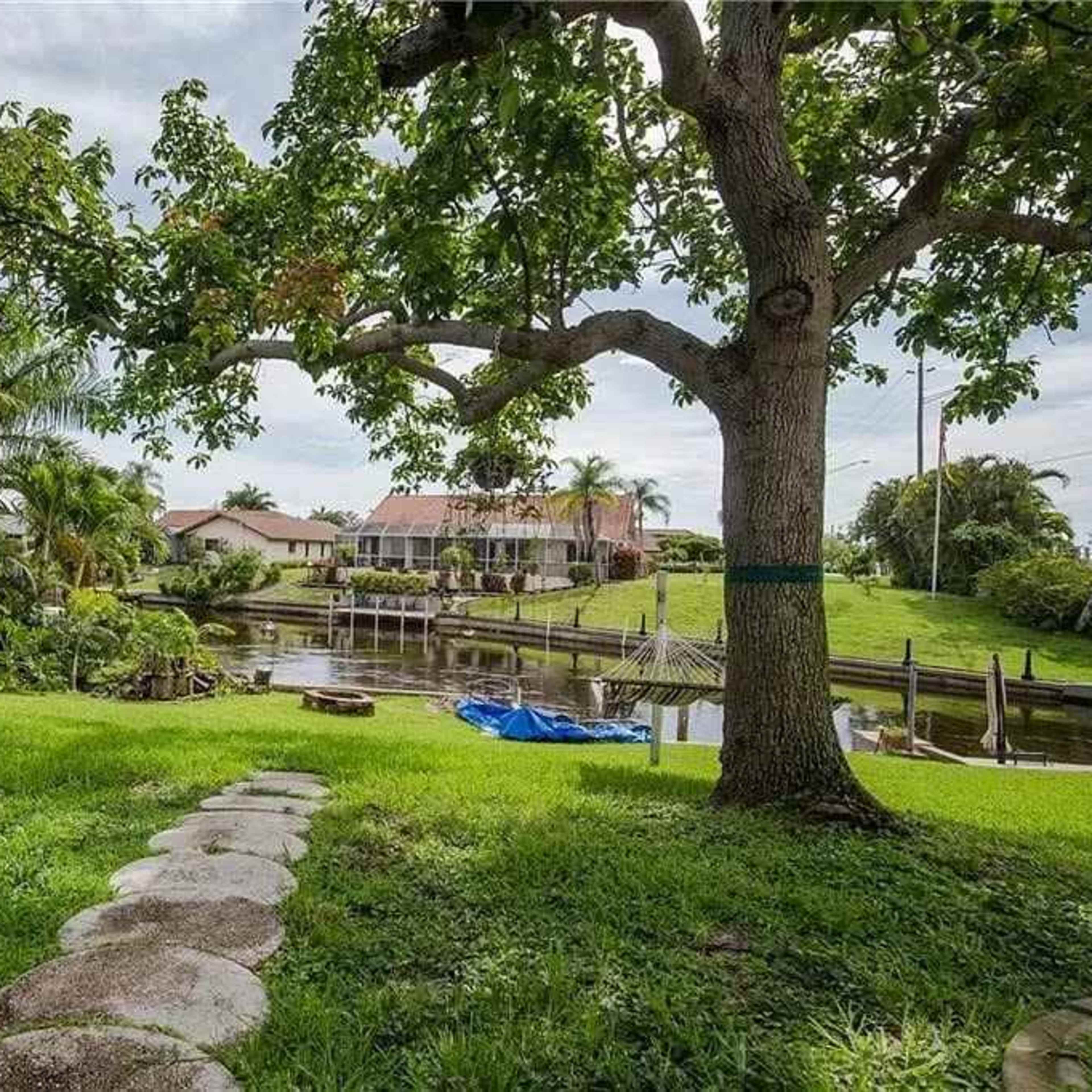 A pathway of stone steps leads through a green yard to a calm waterway bordered by homes and palm trees.