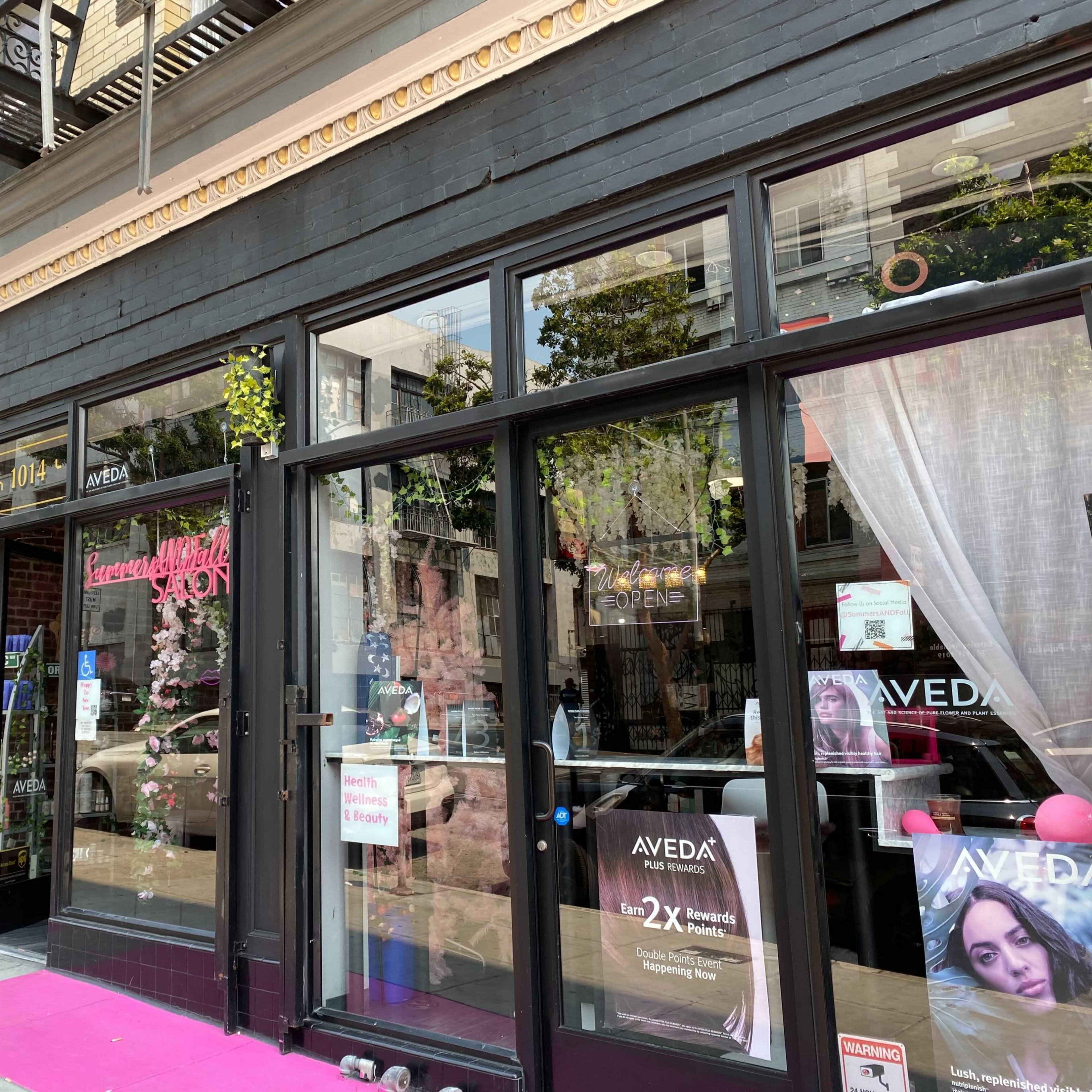 The storefront features a beauty salon with large glass windows, pink carpeting, and signage for Aveda products.