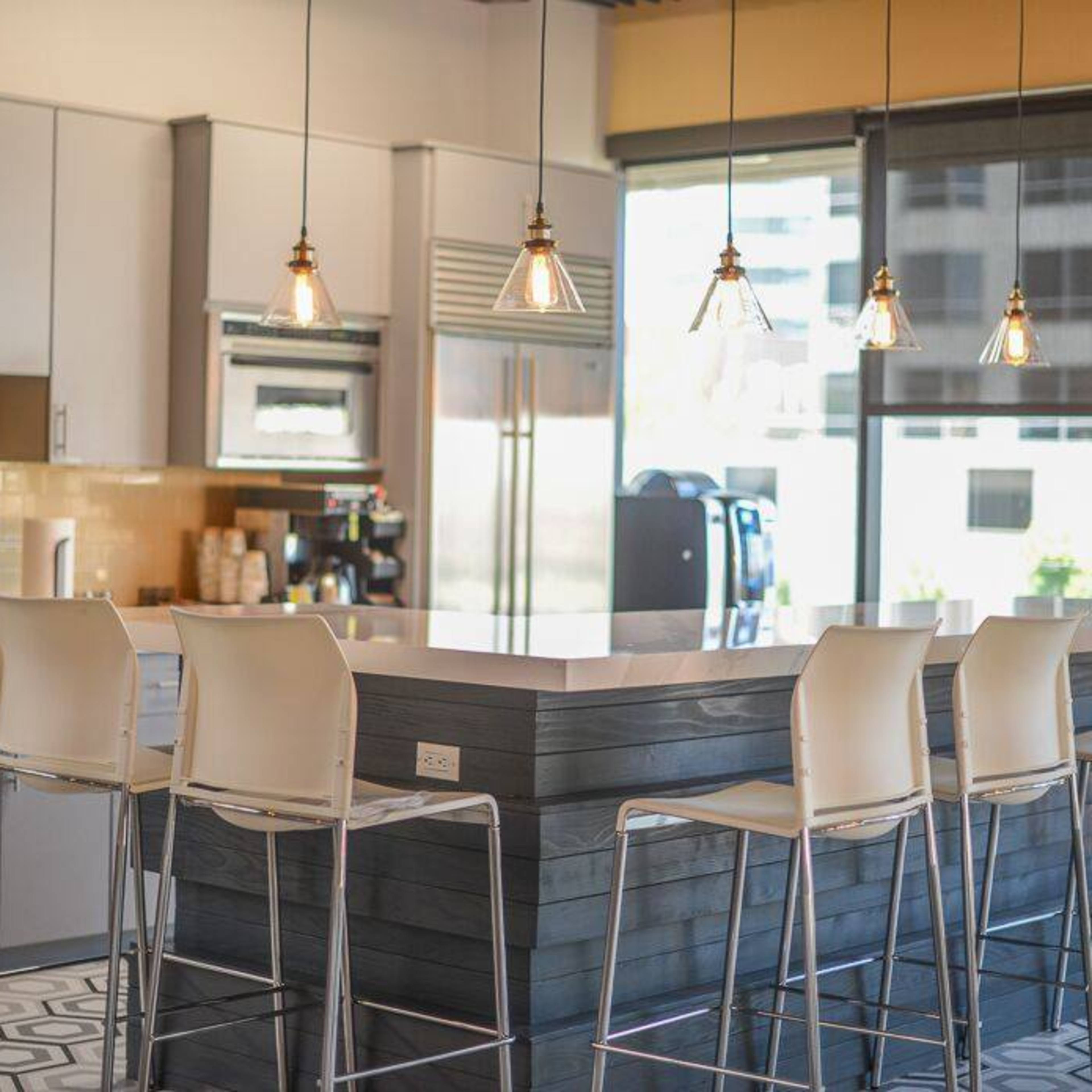 A modern kitchen features a large island with bar seating, pendant lights, and stainless steel appliances.