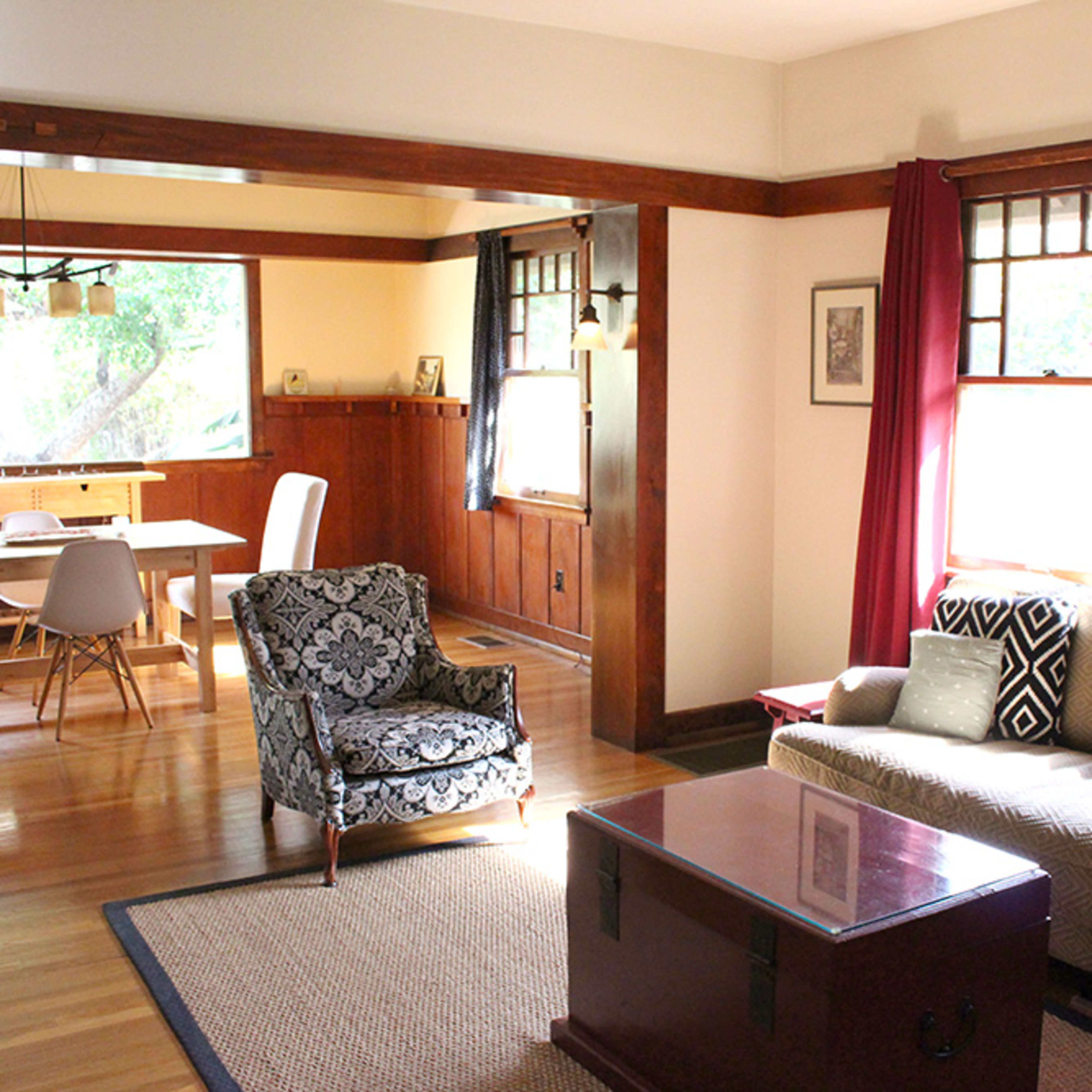 A sunlit living room and dining area featuring a sofa, an armchair, and a wooden dining table.