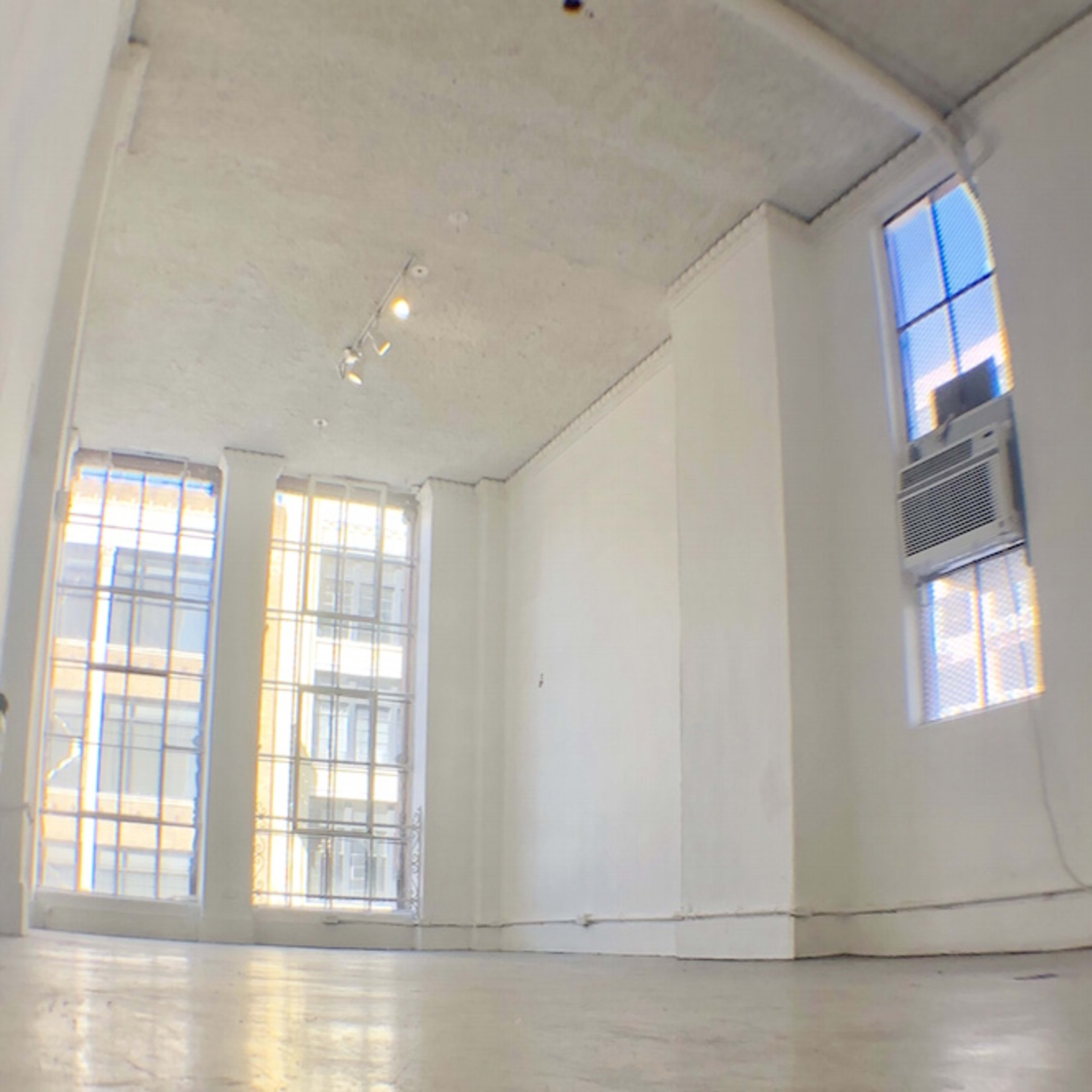 An empty, well-lit room with large windows and an air conditioning unit.