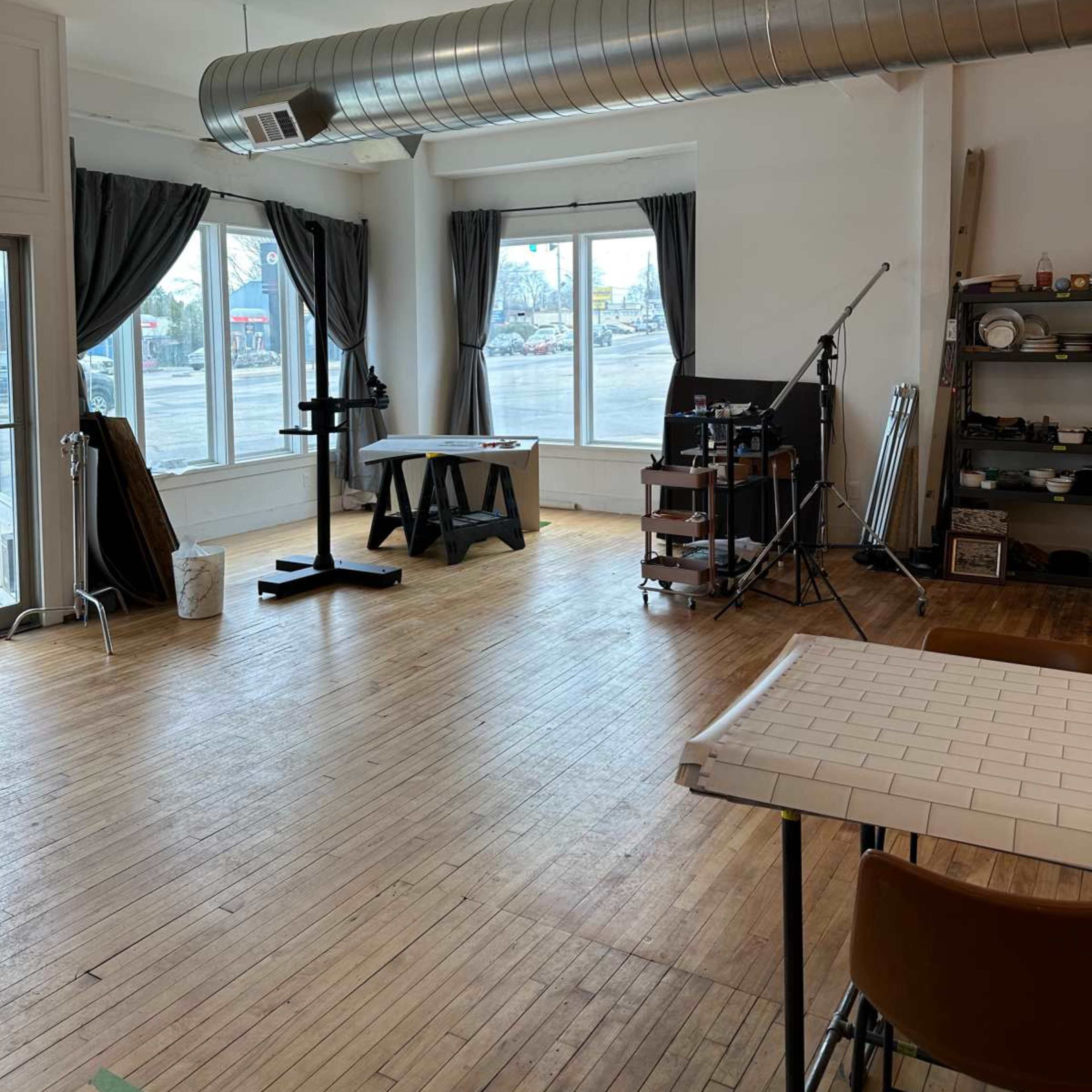 A spacious studio with large windows, wooden flooring, and various equipment arranged around the room.