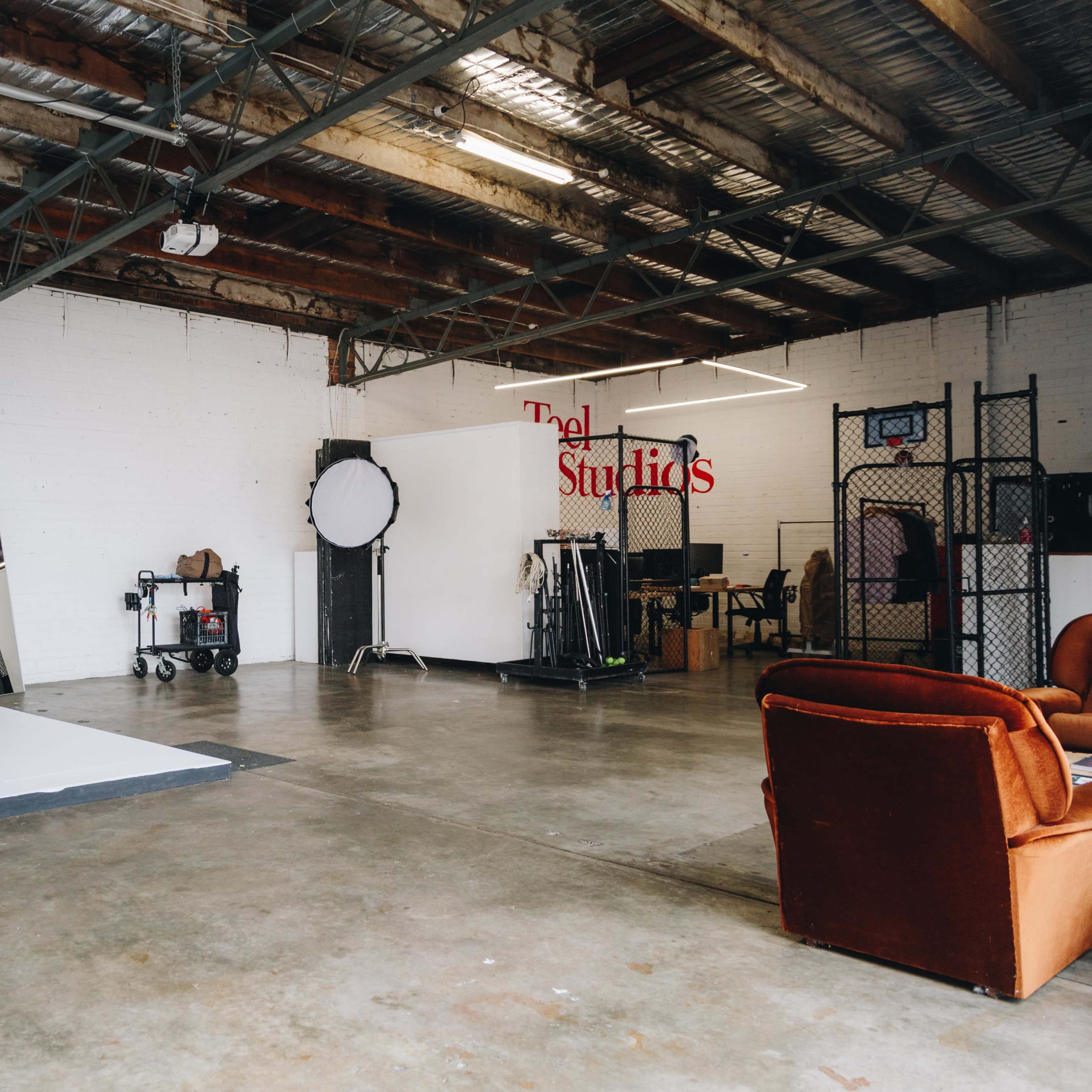 A spacious studio with a large white backdrop, studio equipment, and a brown couch against a concrete floor.