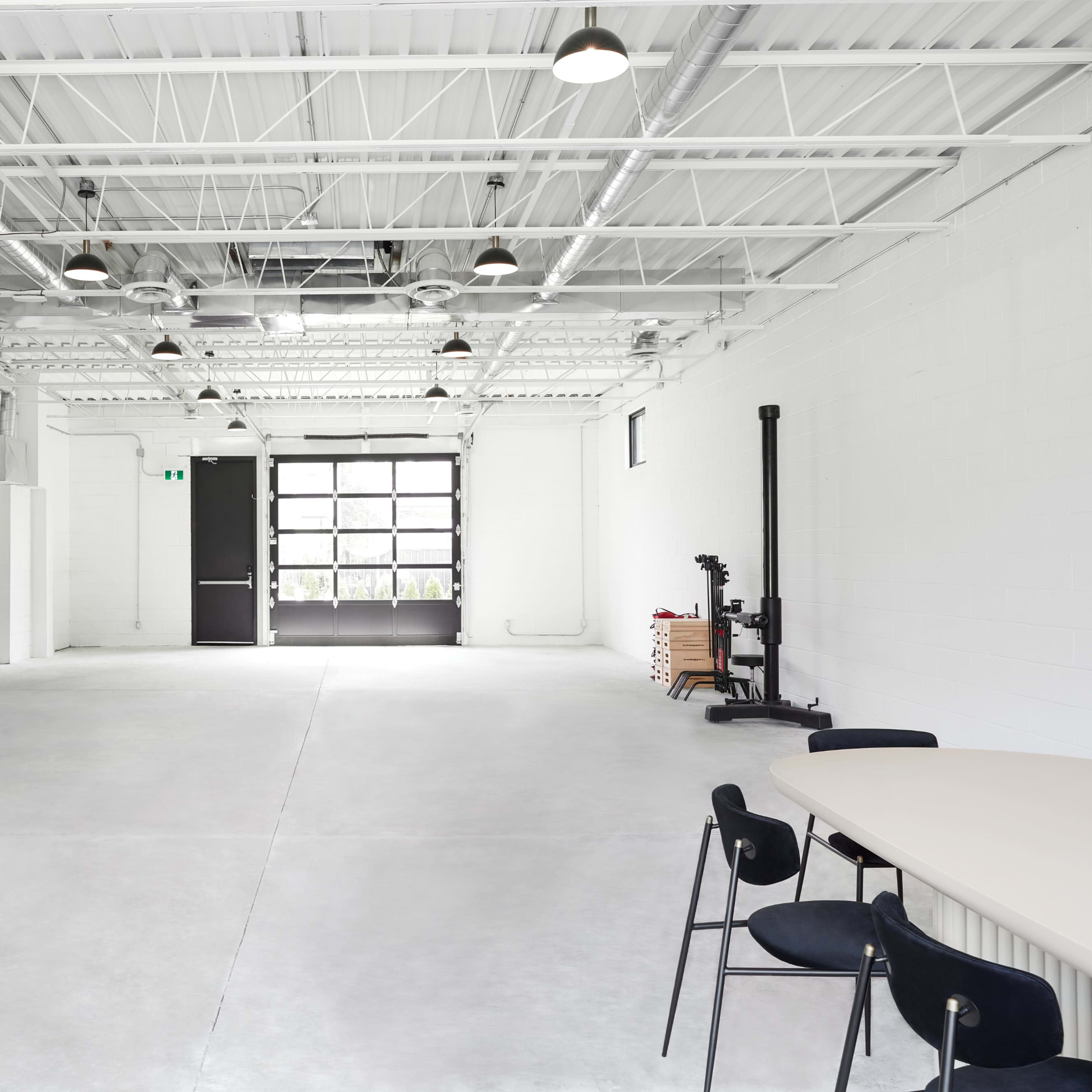 A spacious, empty interior of a modern industrial-style room with a kitchen area on the left and a large garage door at the far end.