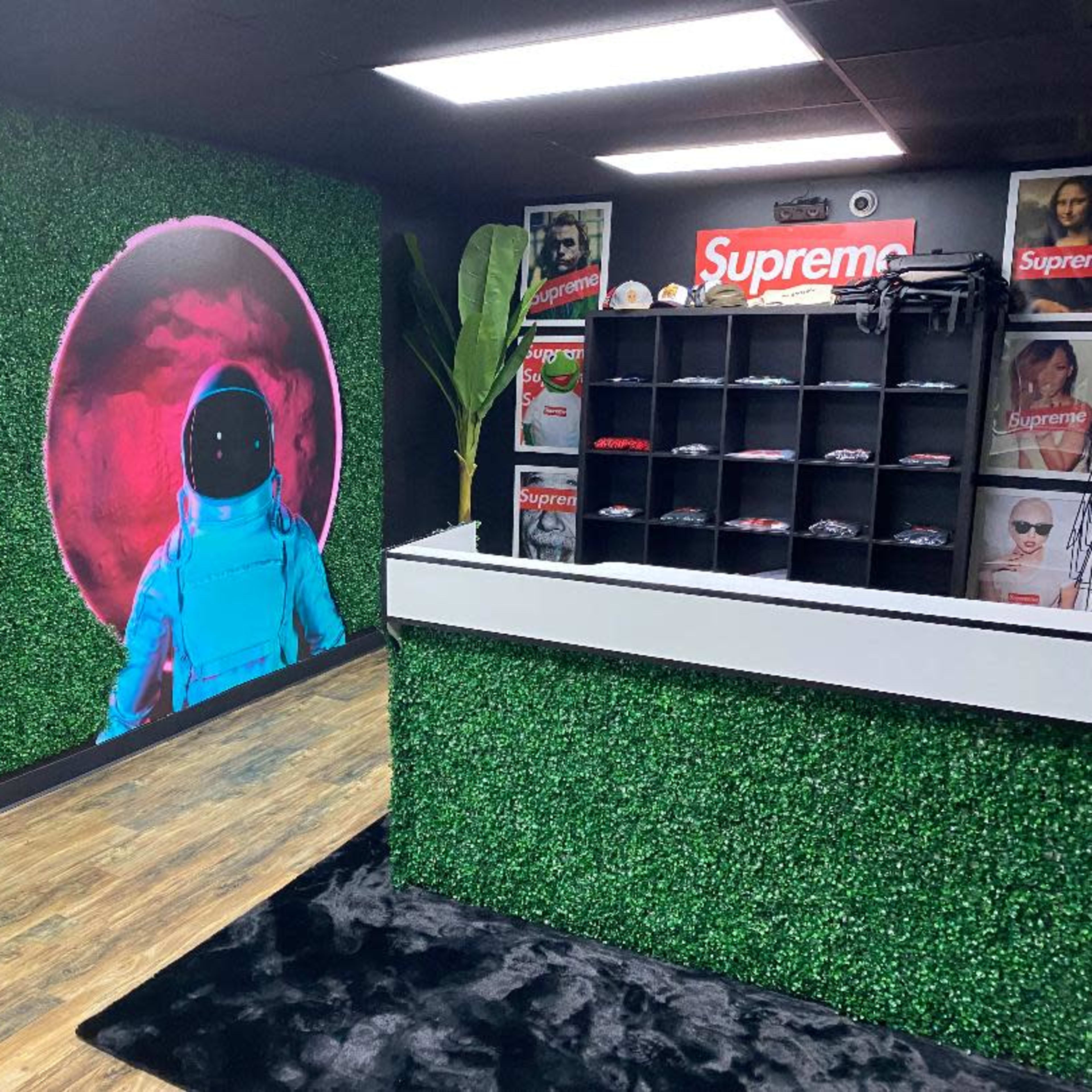 A retail space with green artificial grass walls, featuring a large astronaut mural and a counter displaying clothing items.