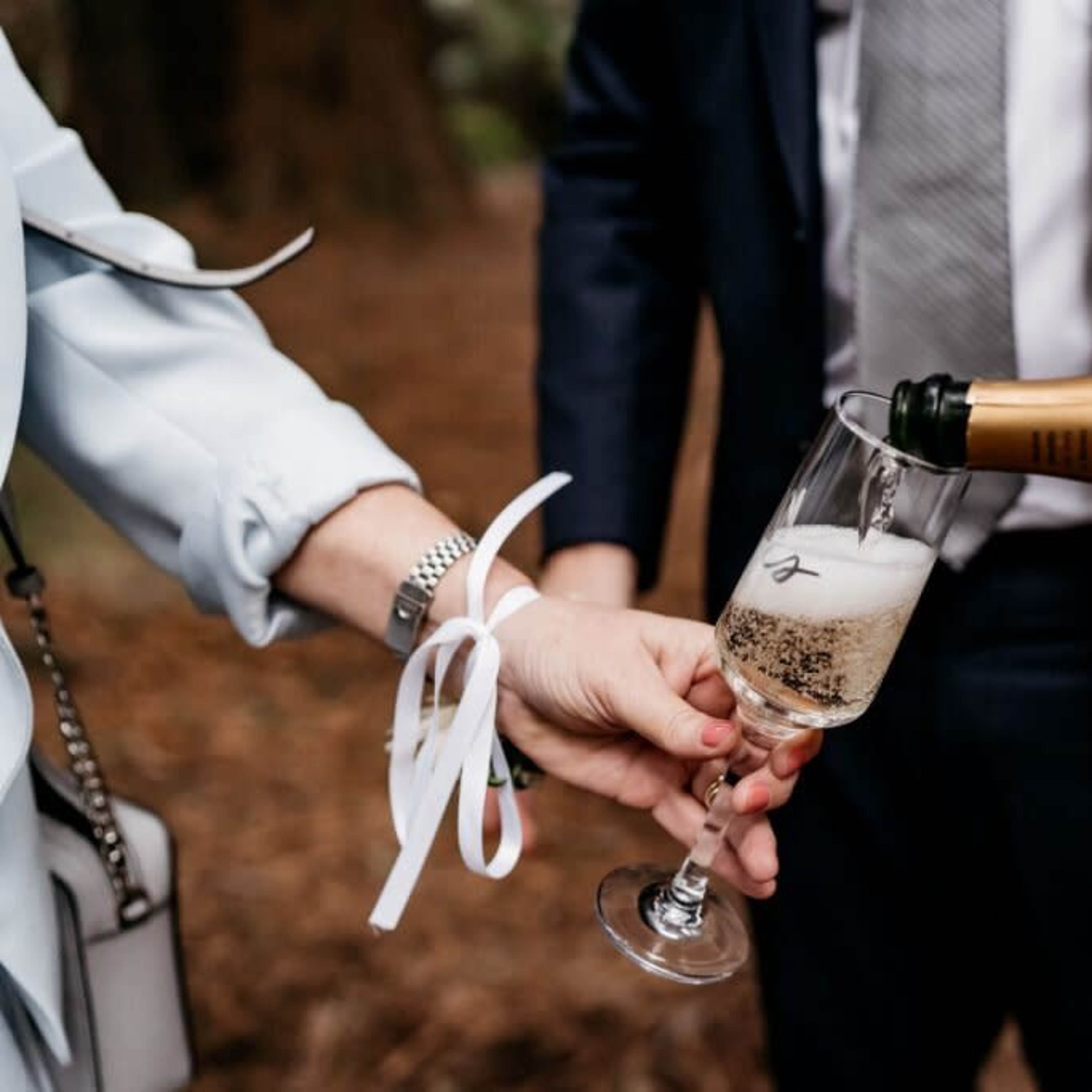 A glass is being filled with champagne from a bottle in a wooded setting.