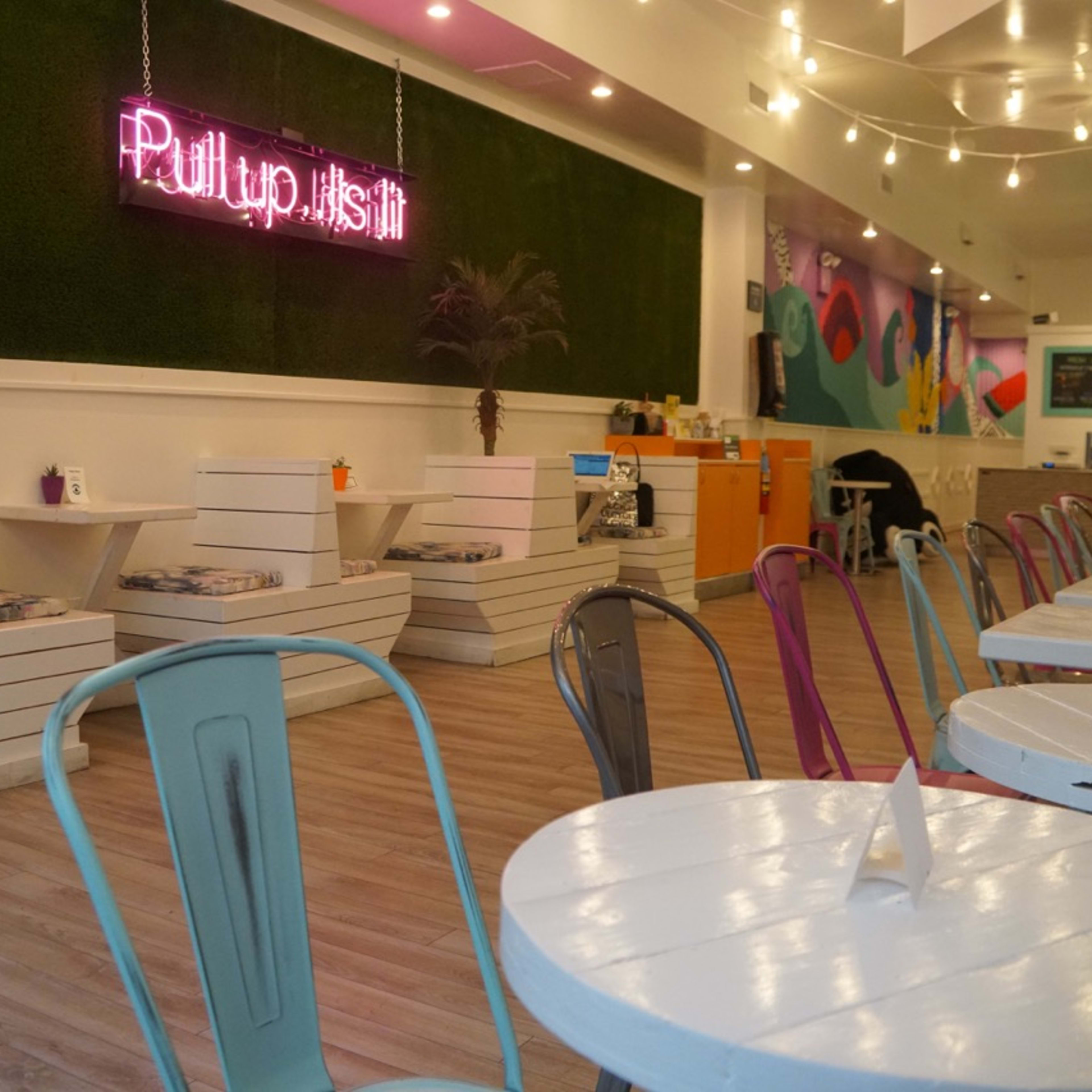 The interior of a café features colorful chairs and minimalist seating areas with neon signage on a green wall.