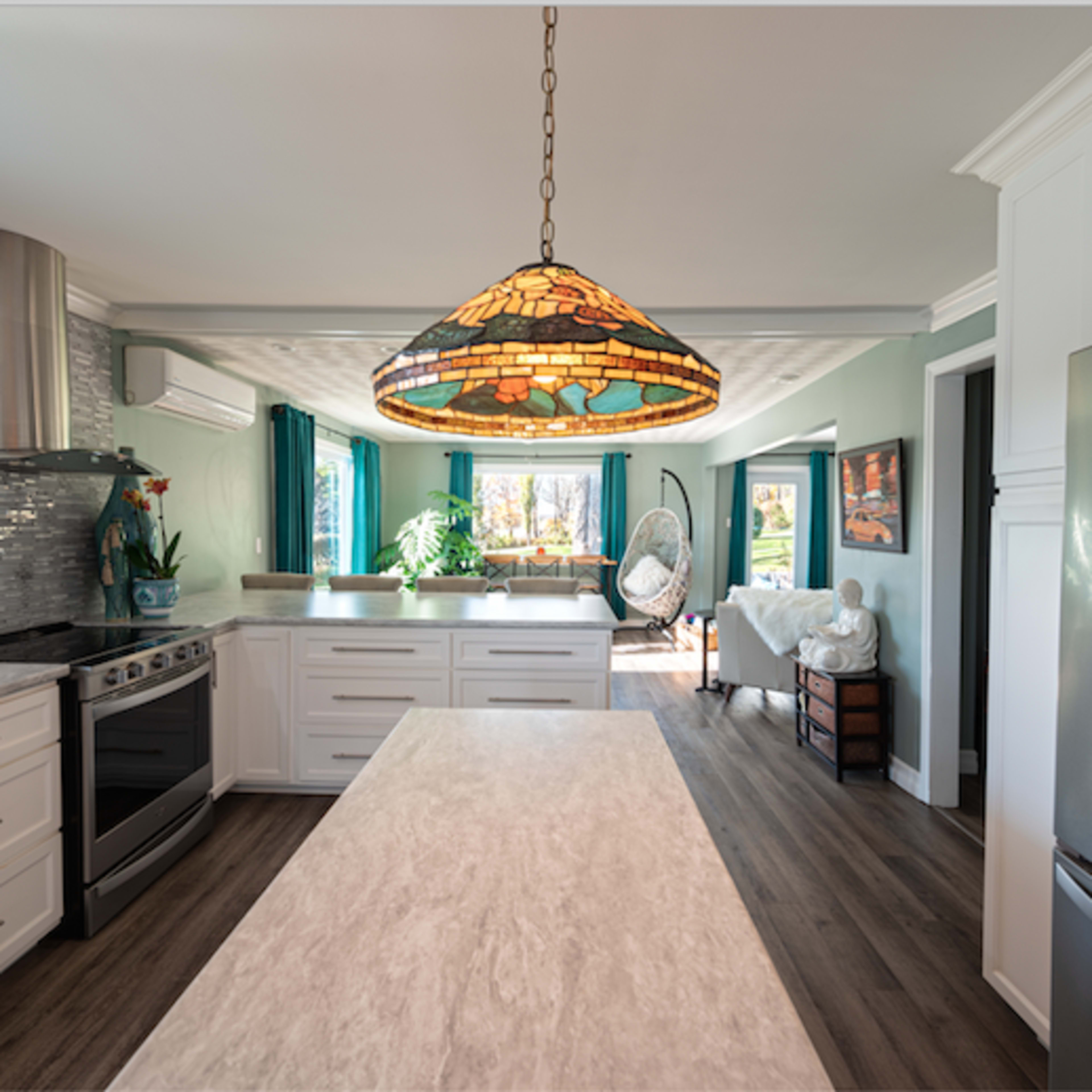 A modern kitchen features a large island with a marble countertop, stainless steel appliances, and a stained glass pendant light.