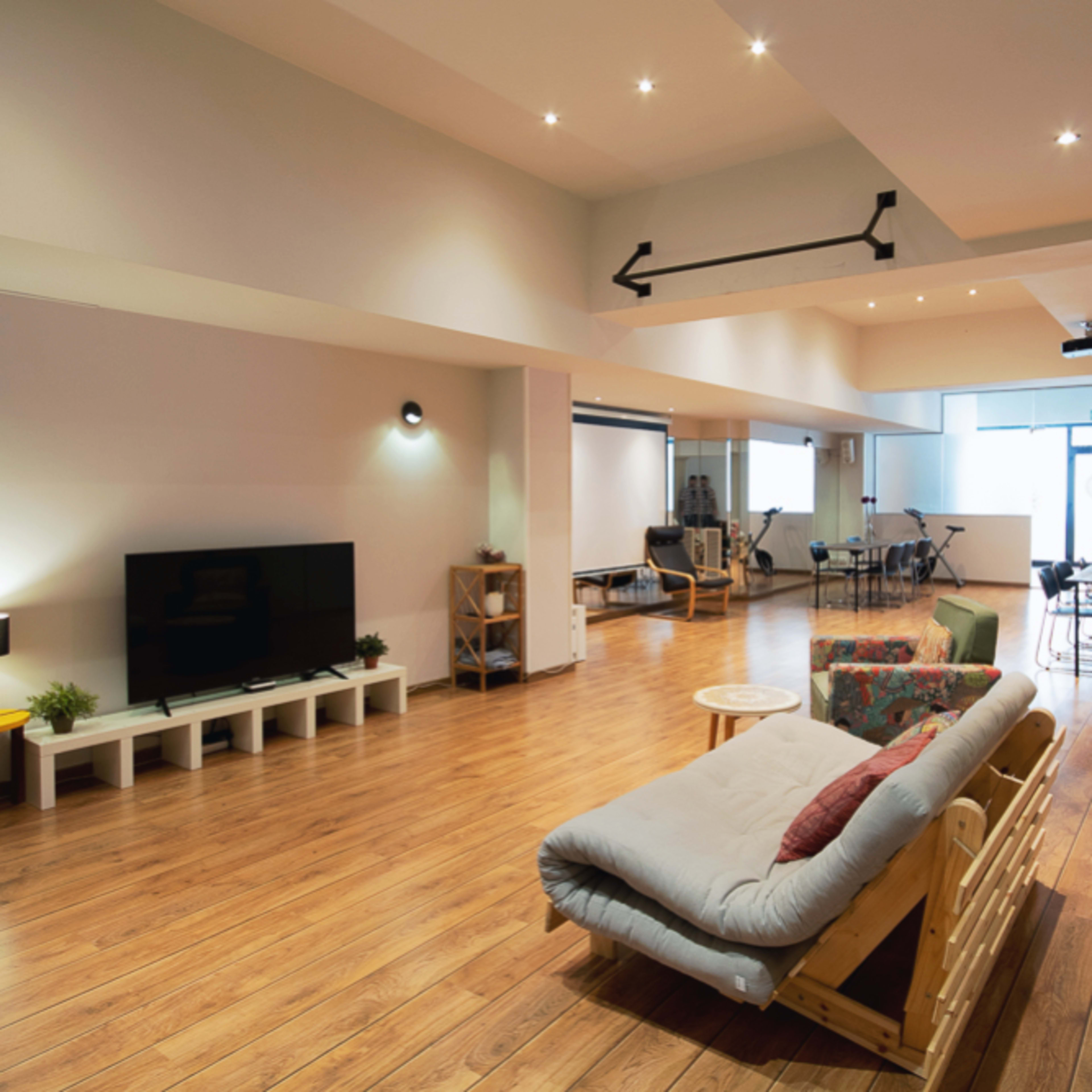 A spacious, modern living room features wooden flooring, a large TV, comfortable sofas, and ample natural light from windows.
