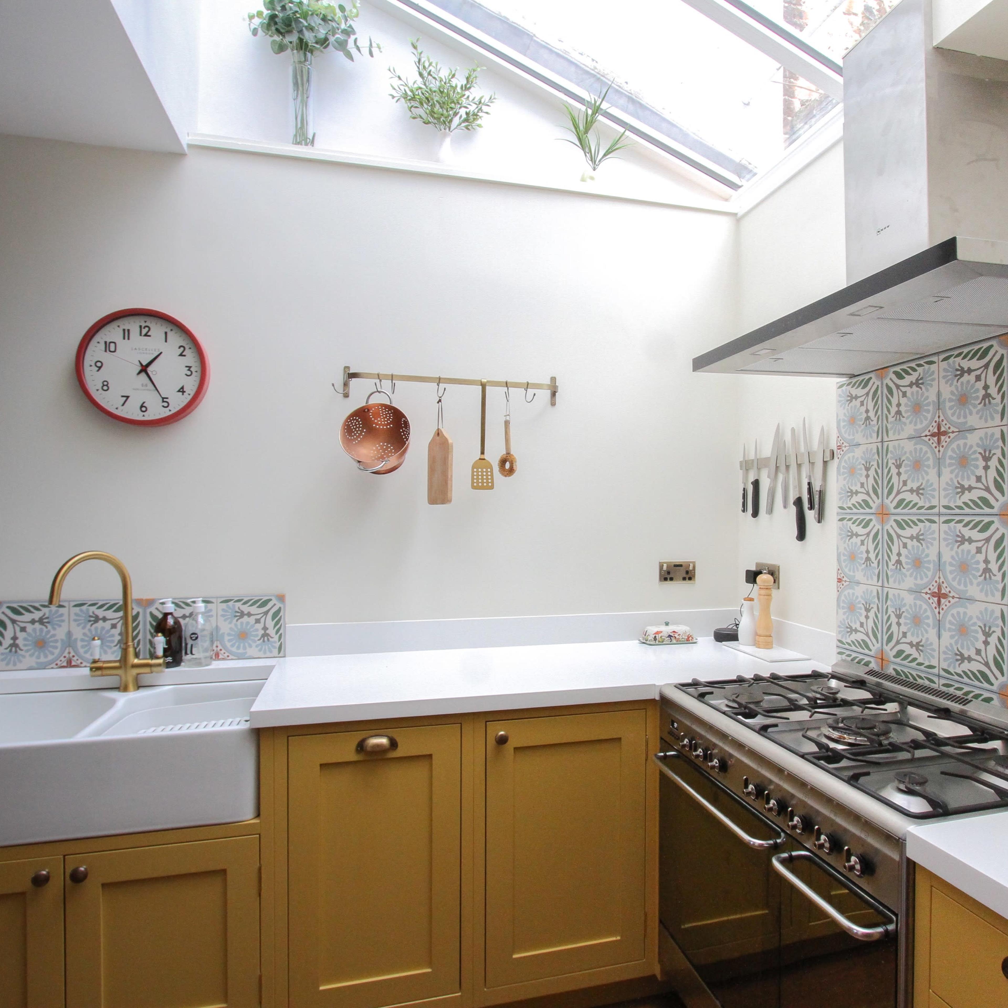 A modern kitchen featuring a mix of yellow cabinets, a white countertop, a stainless steel oven, and decorative patterned tiles behind the stove.
