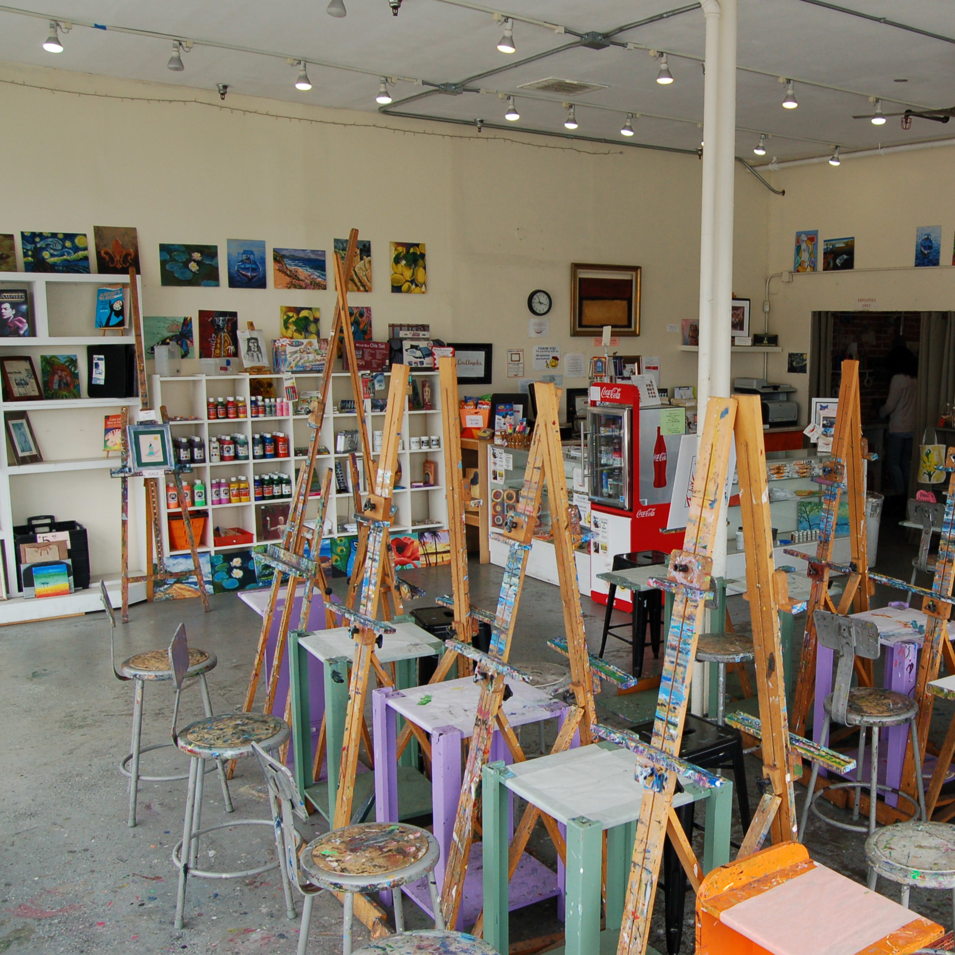An artist studio filled with easels, stools, and shelves stocked with art supplies and paintings on the walls.