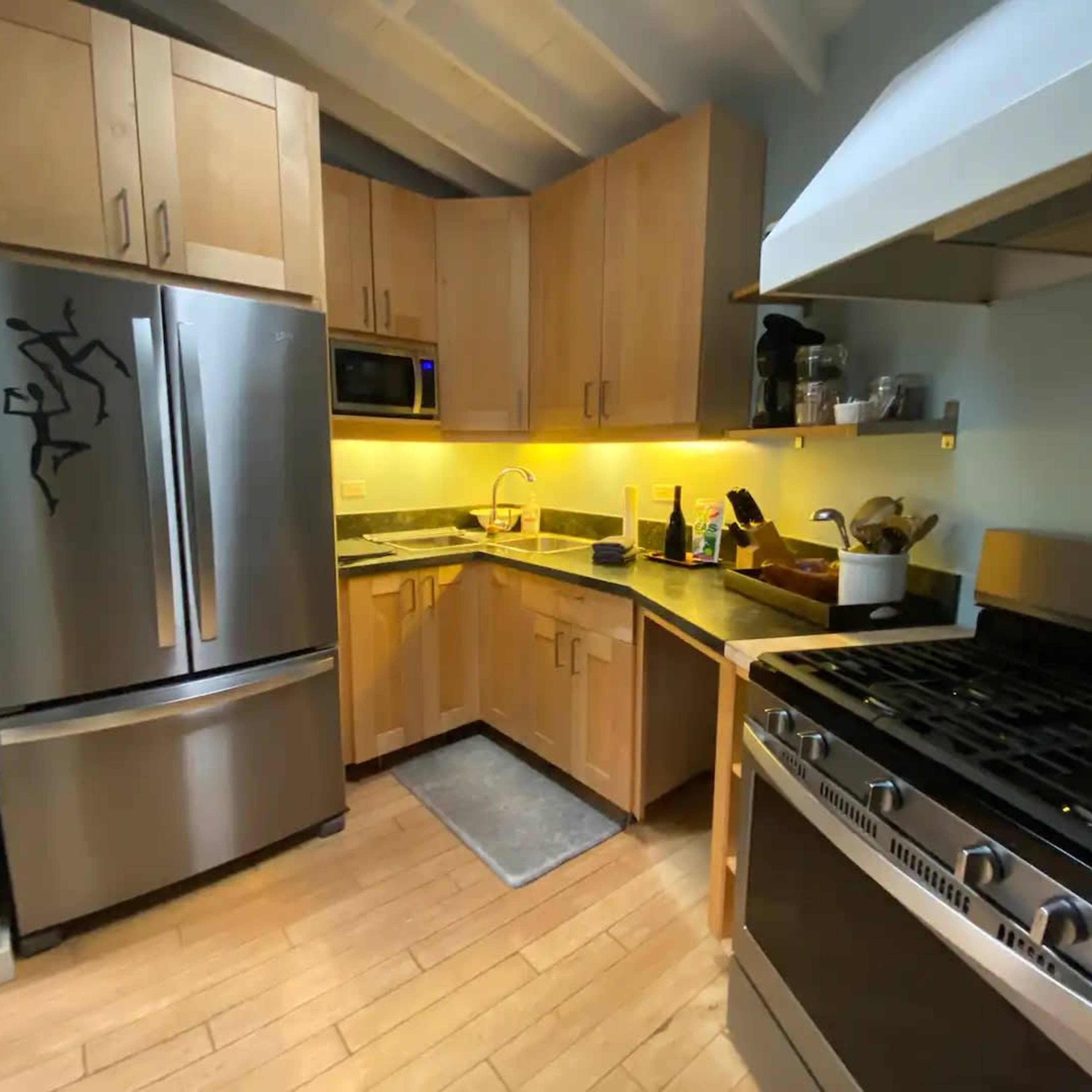 A modern kitchen features stainless steel appliances, light wood cabinetry, and a gray rug on a hardwood floor.