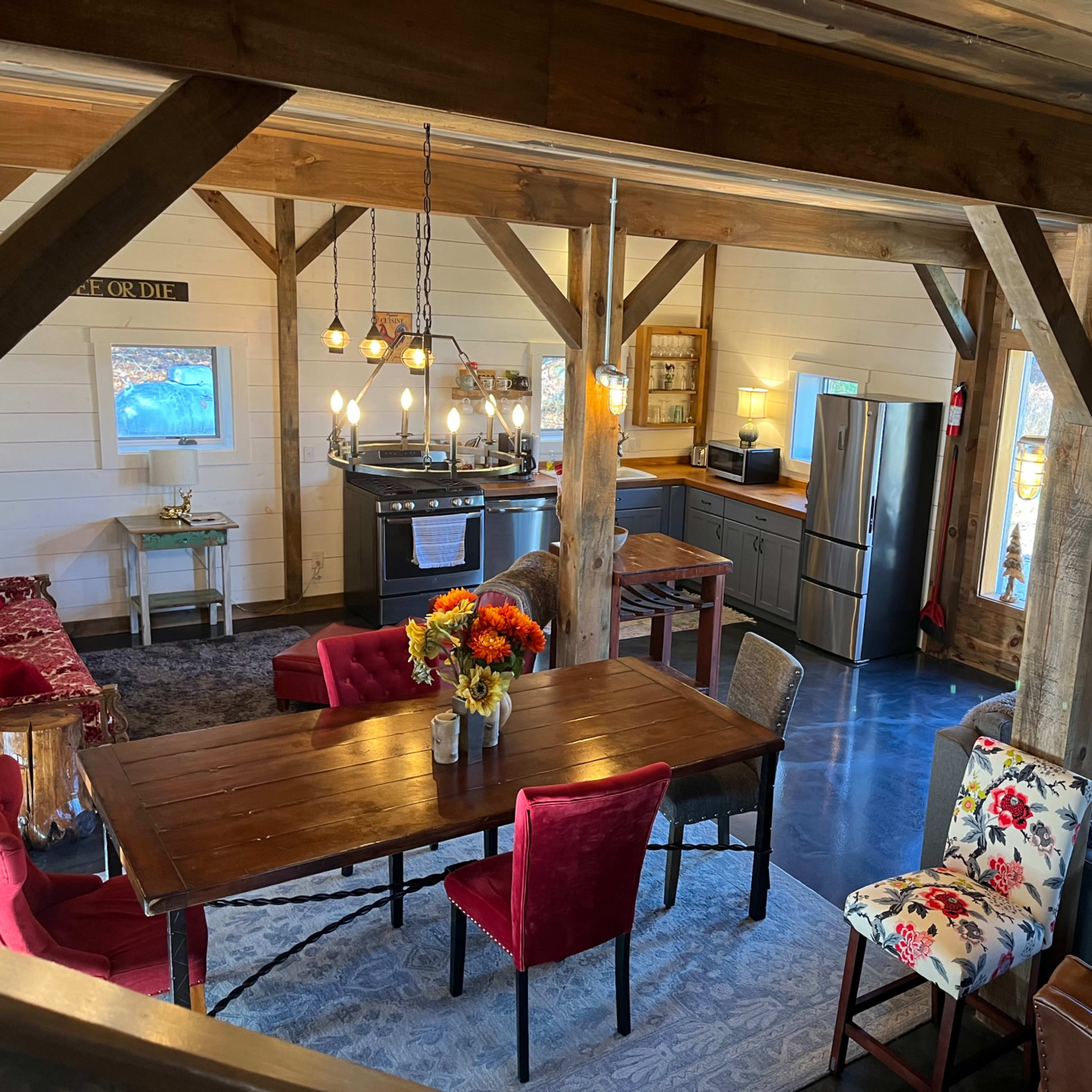 A rustic interior of a cabin featuring a wooden dining table, chairs, and a living area with a couch, along with a kitchen equipped with modern appliances.