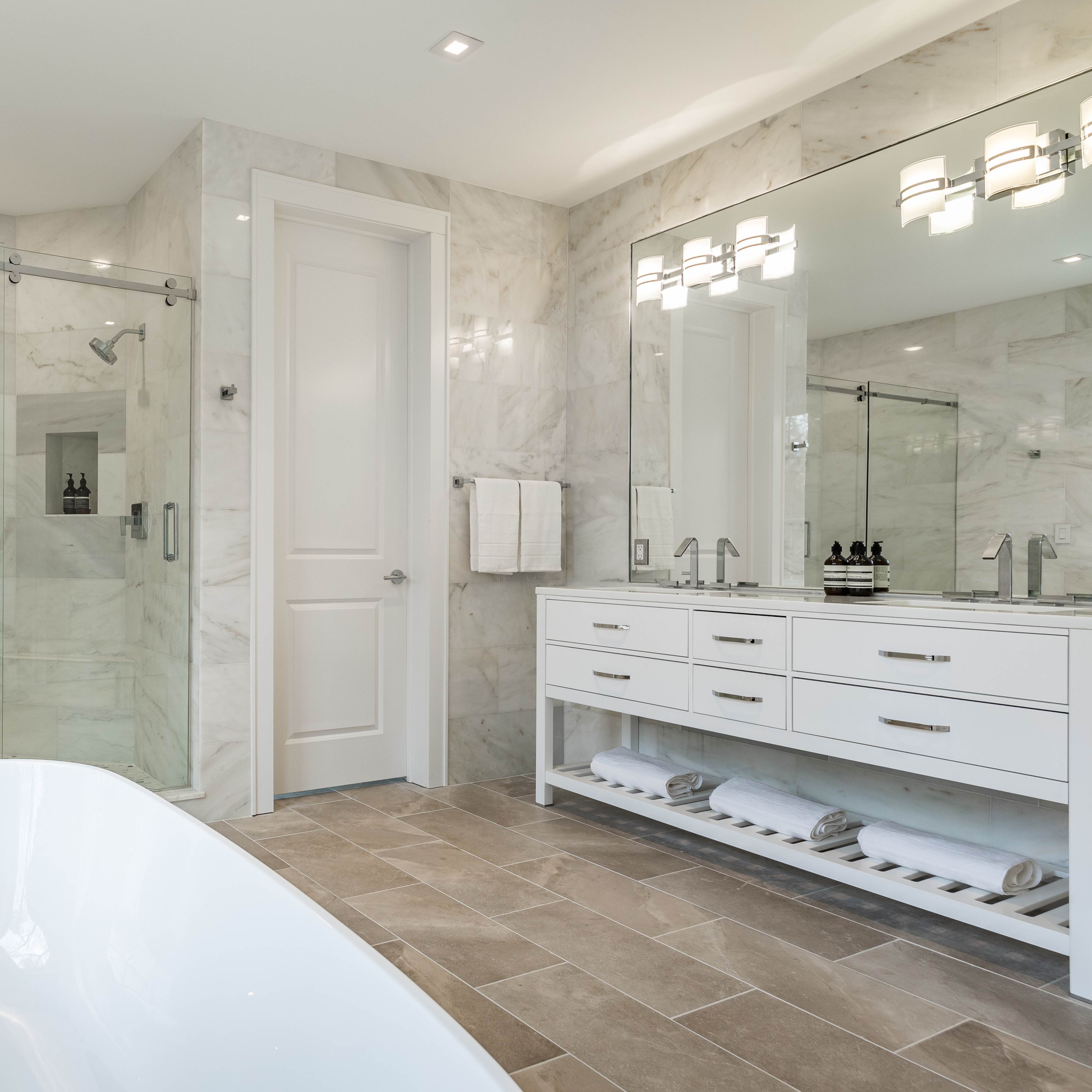A modern bathroom featuring a freestanding bathtub, a glass-enclosed shower, and a double vanity with mirrors and elegant lighting.