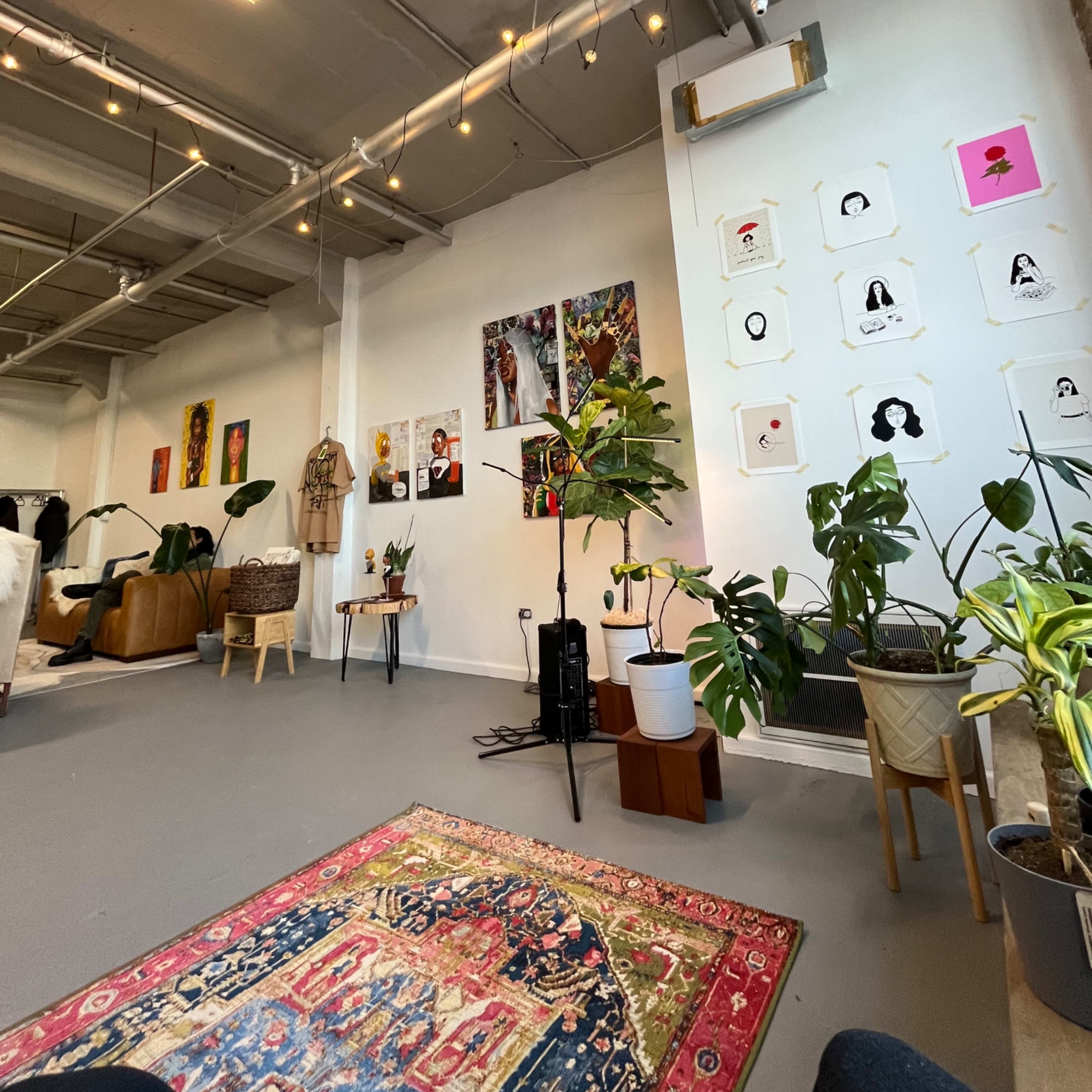 A spacious indoor area with a variety of potted plants, artworks on the walls, and a decorative rug on the floor.