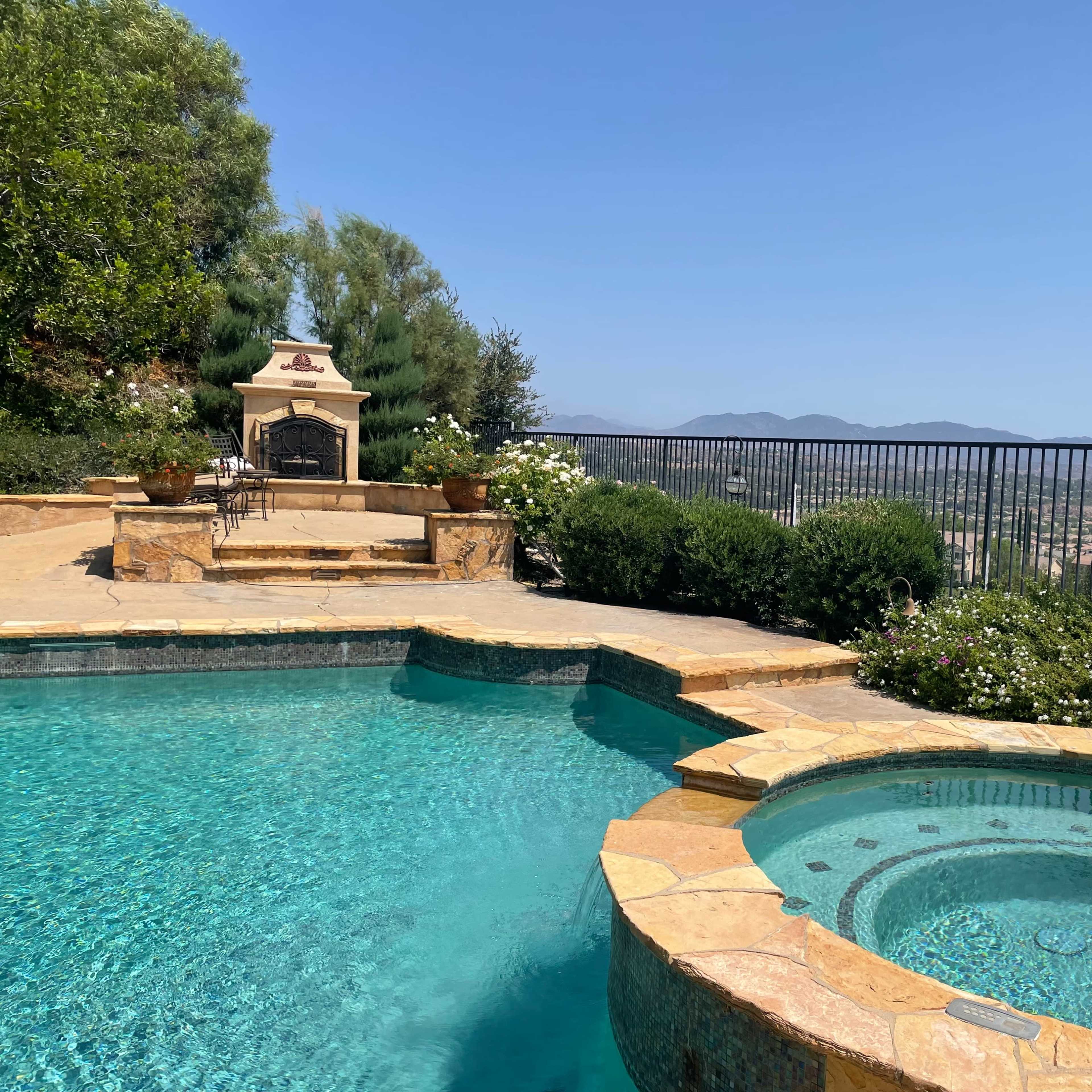 A backyard featuring a pool and a hot tub with a view of distant mountains and a clear blue sky.
