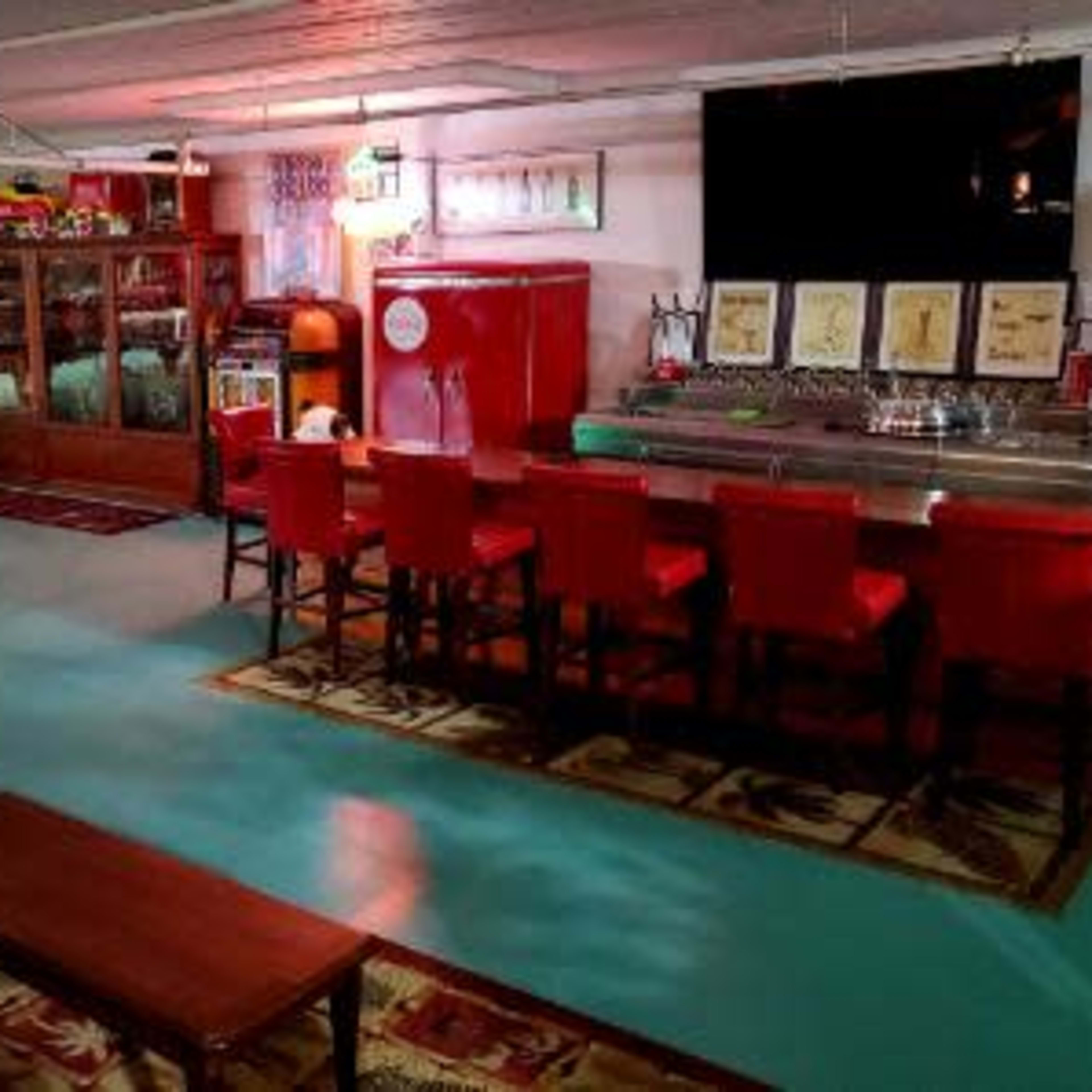 A retro-themed basement featuring a Coca-Cola vending machine, a bar with red stools, a large glass cabinet, and various vintage decorations.