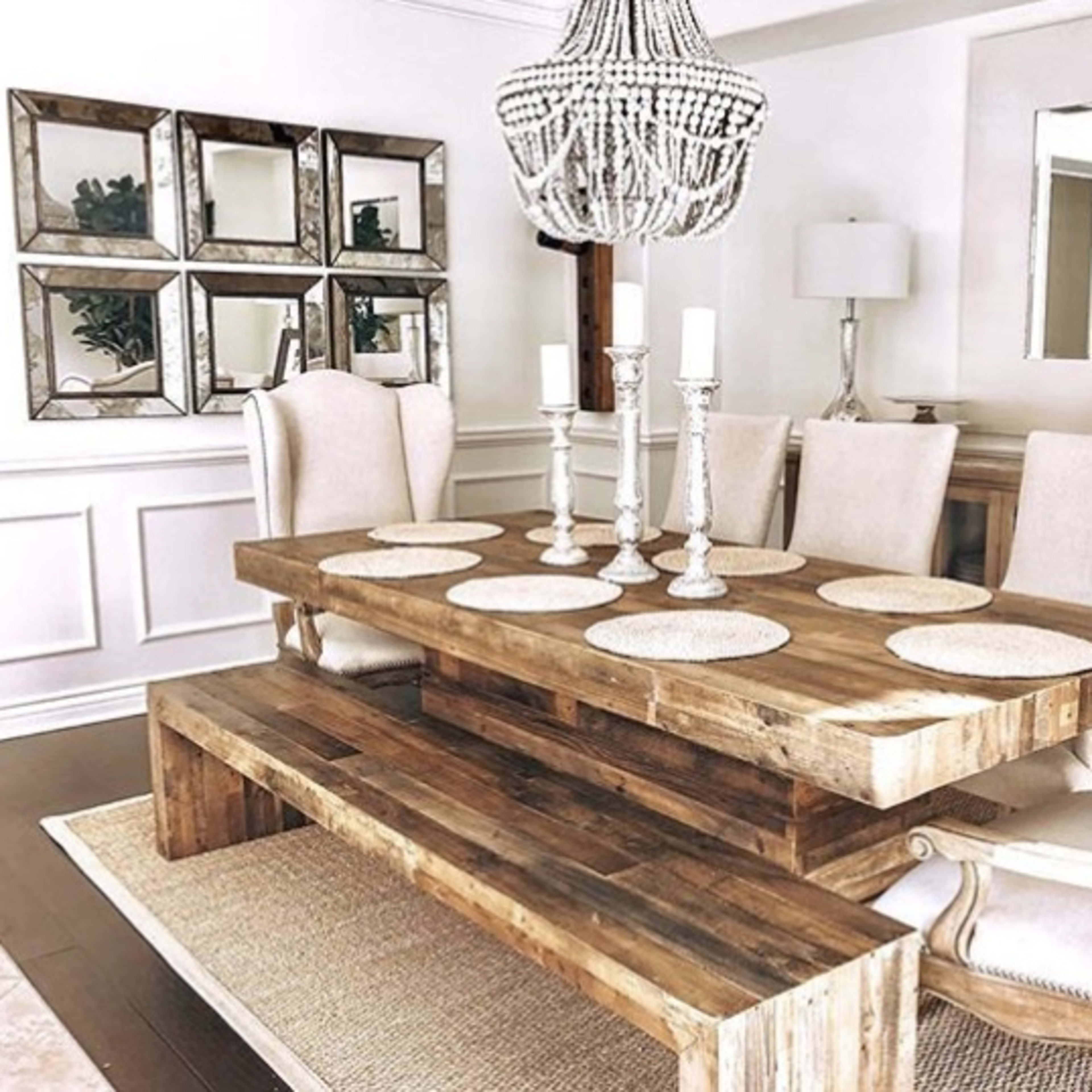 A wooden dining table with upholstered chairs, surrounded by decorative mirrors and candle holders, is set in a bright, elegantly arranged dining room.