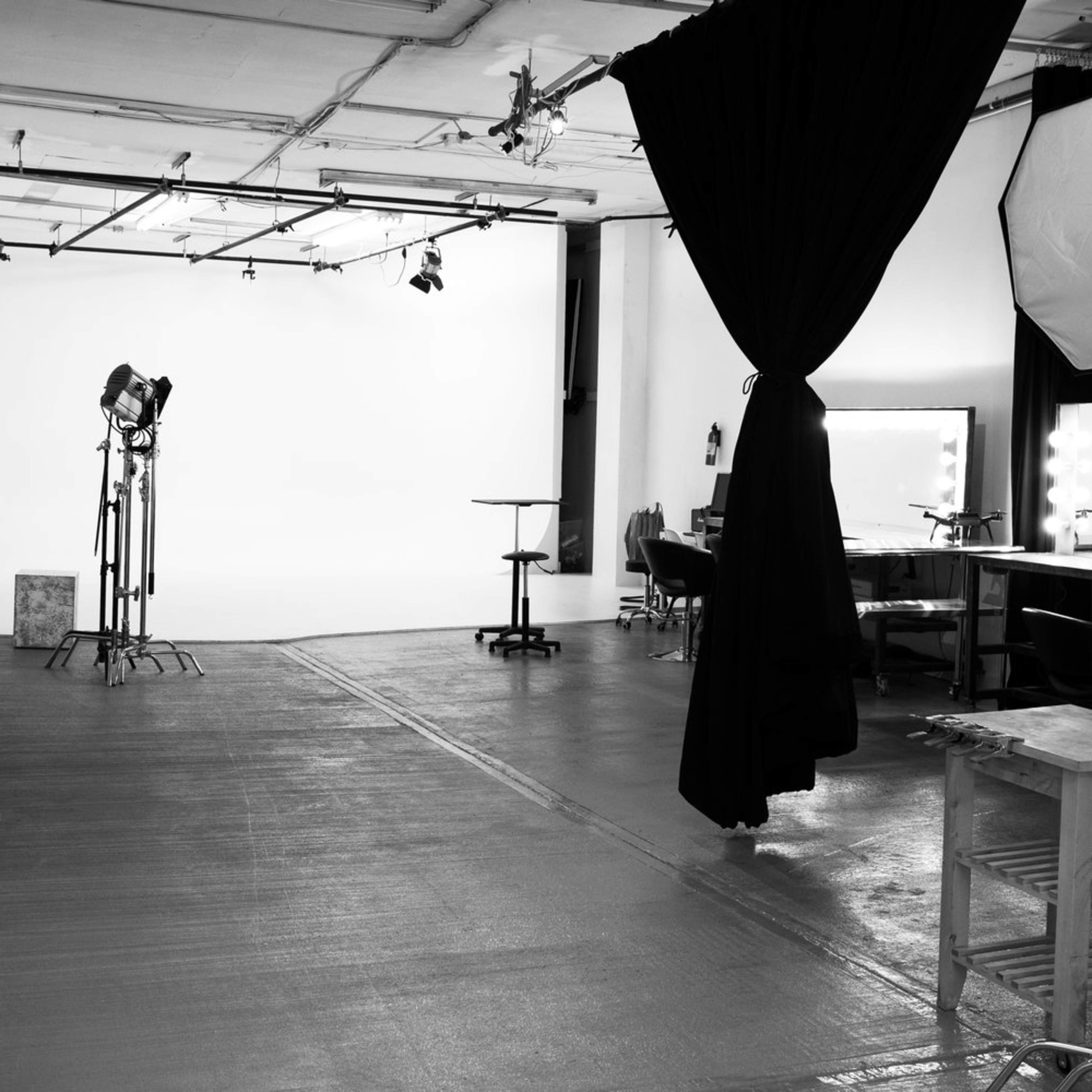 A spacious photography studio with a white backdrop, lighting equipment, and various props arranged along the sides.