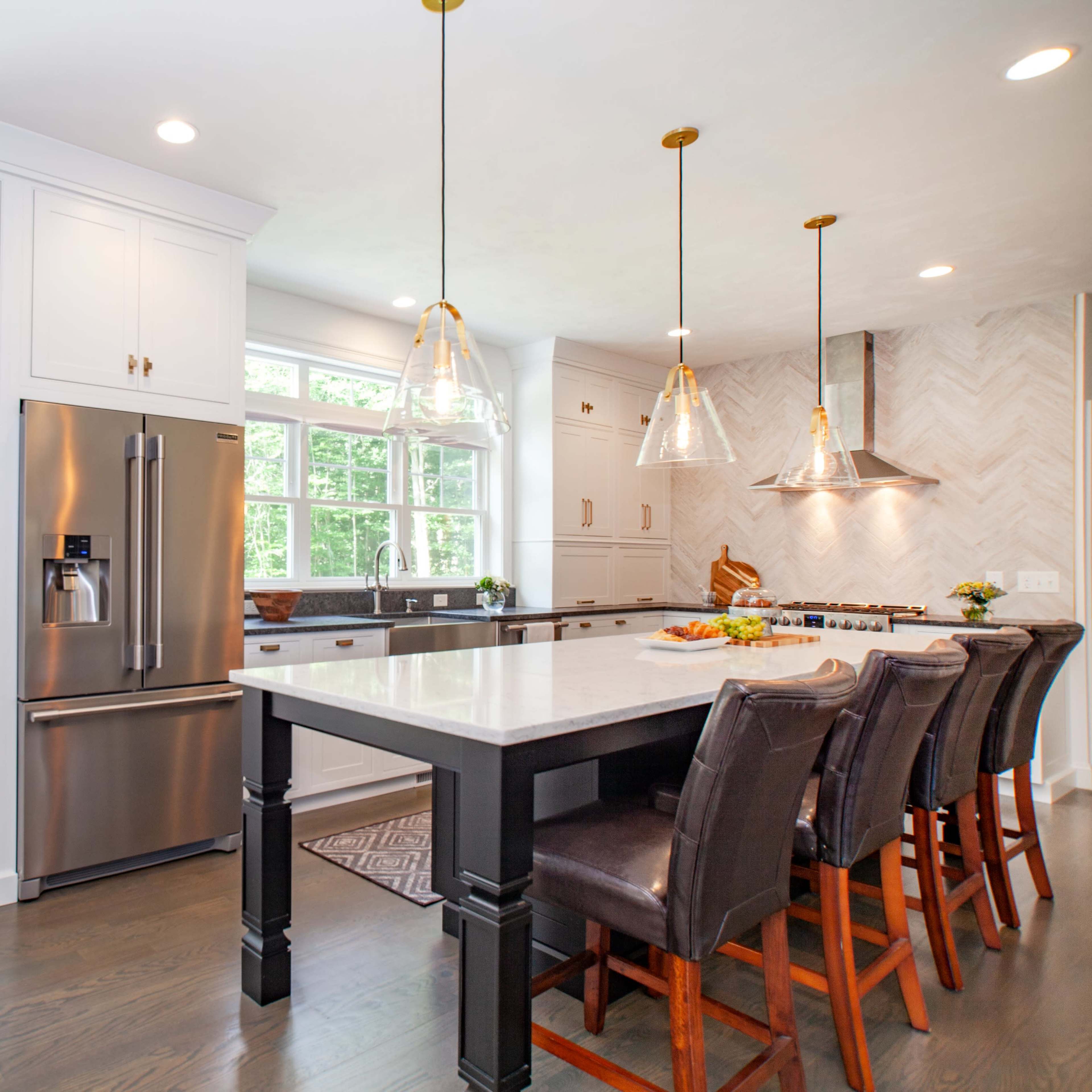 A modern kitchen features a large island with bar seating, stainless steel appliances, white cabinetry, and ample natural light from large windows.