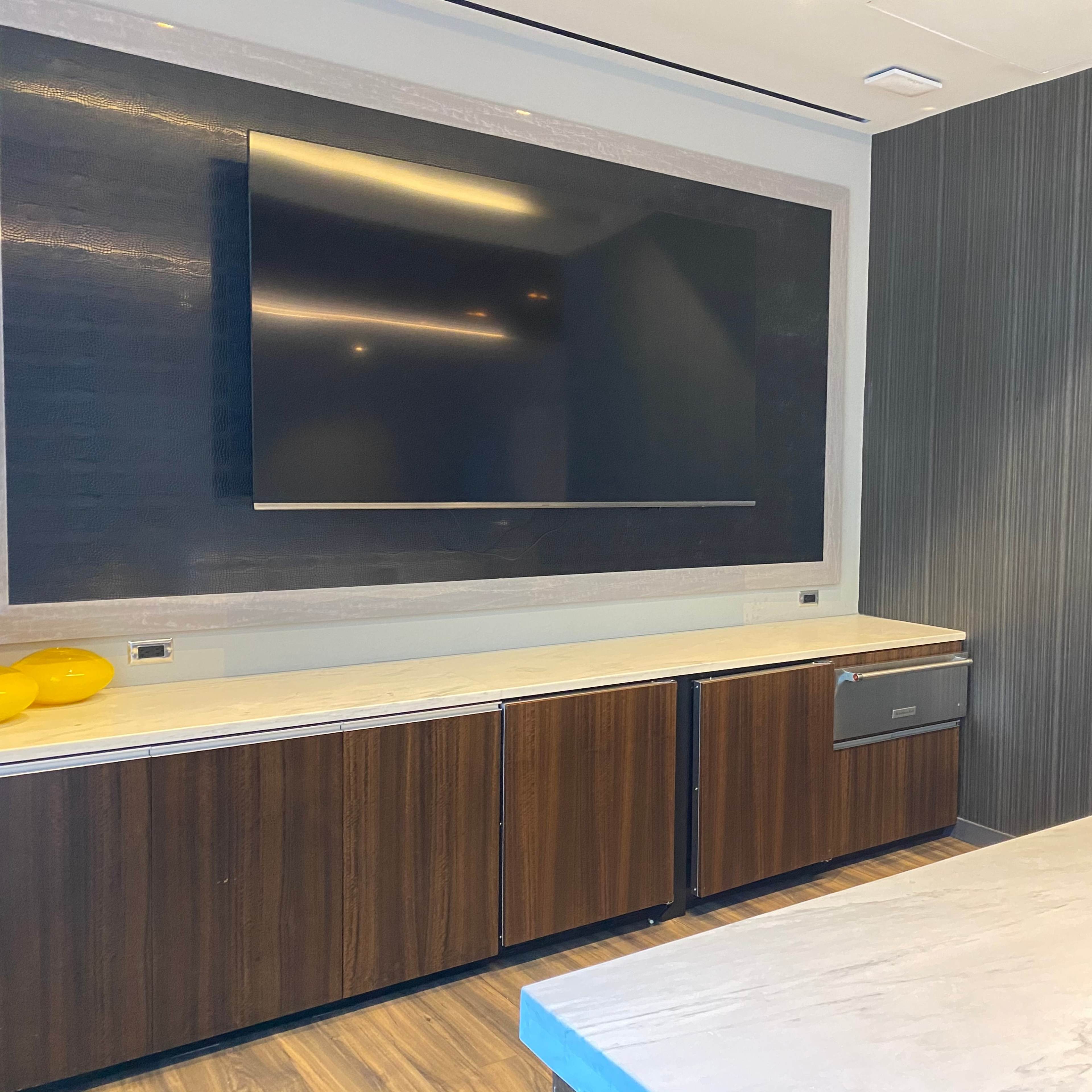 A modern room with a large flat-screen TV mounted on the wall above a marble countertop and wooden cabinetry.