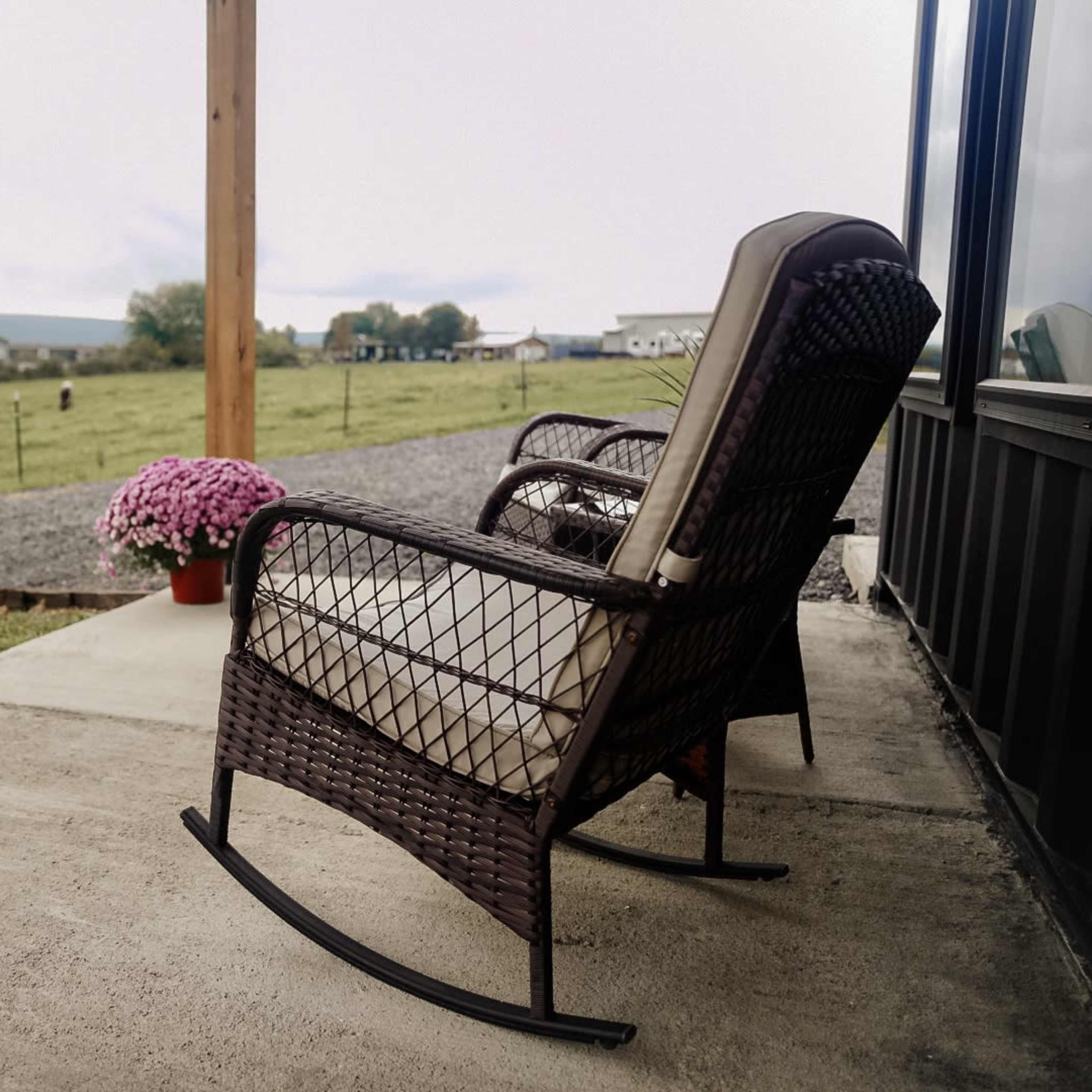 A rocking chair on a porch overlooks a grassy field and a distant farm.
