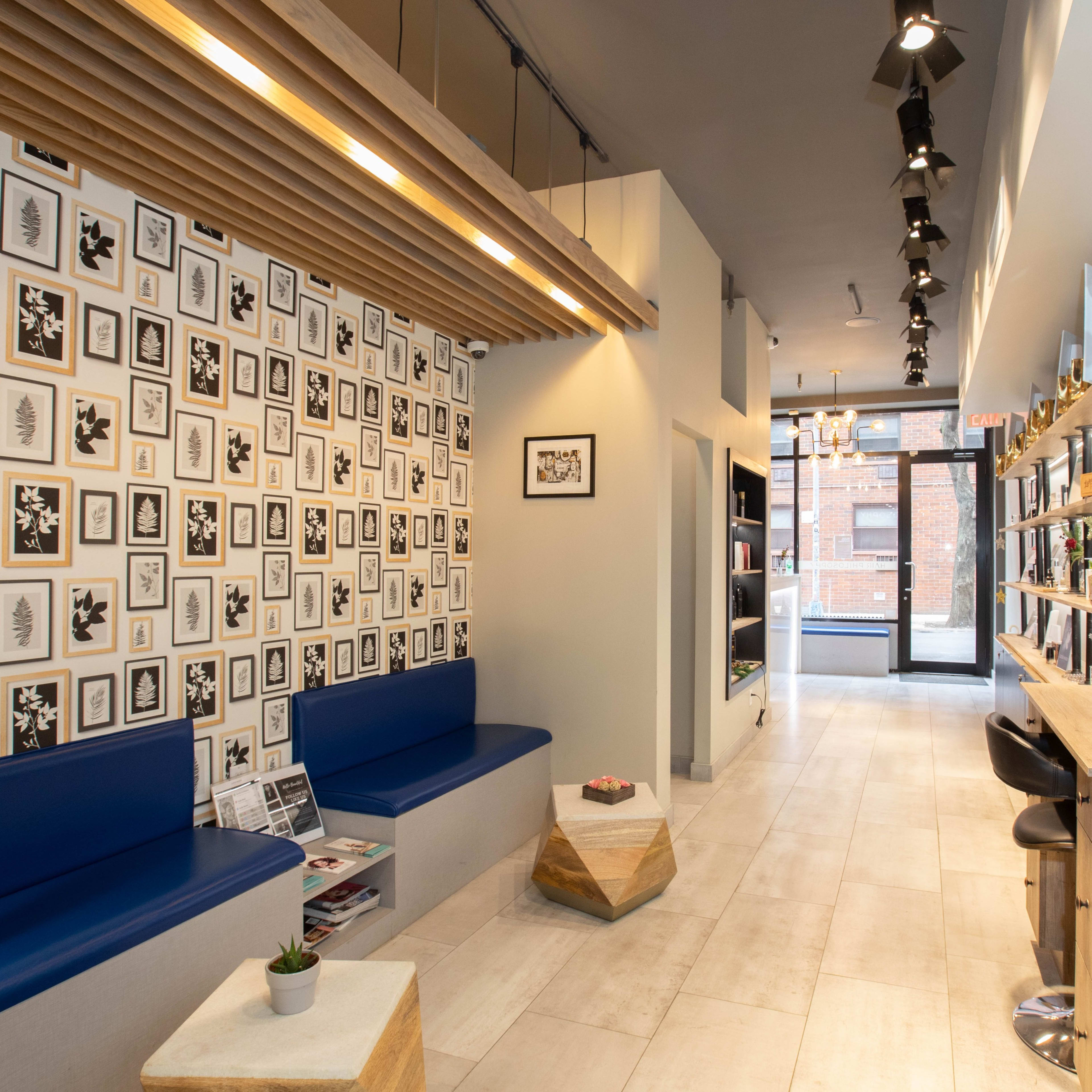 A modern interior space with a patterned wall of framed artworks, blue seating, and a sleek bar area lined with lights.
