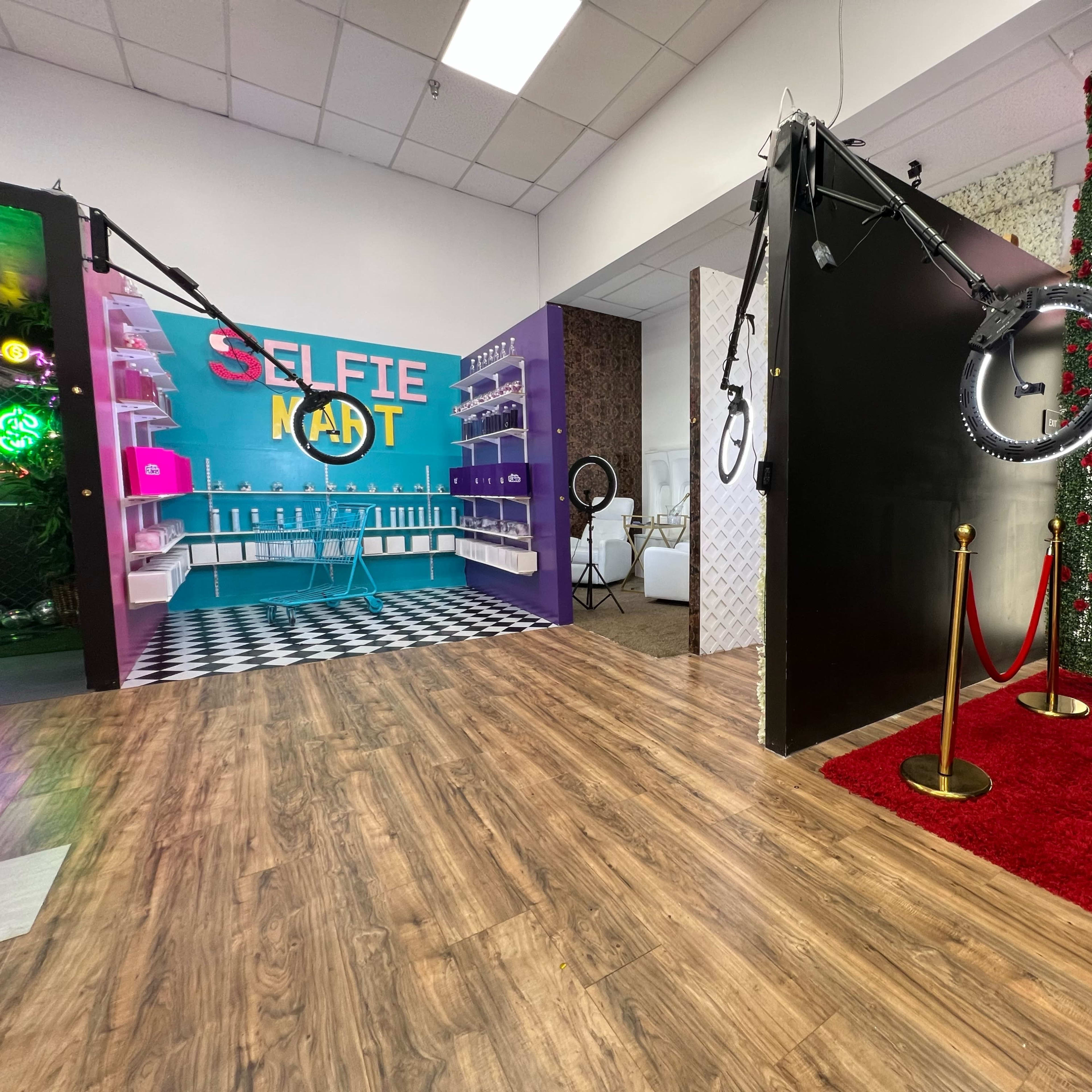A brightly colored selfie station with a backdrop and lighting equipment, alongside a red carpet entrance and a floral wall.