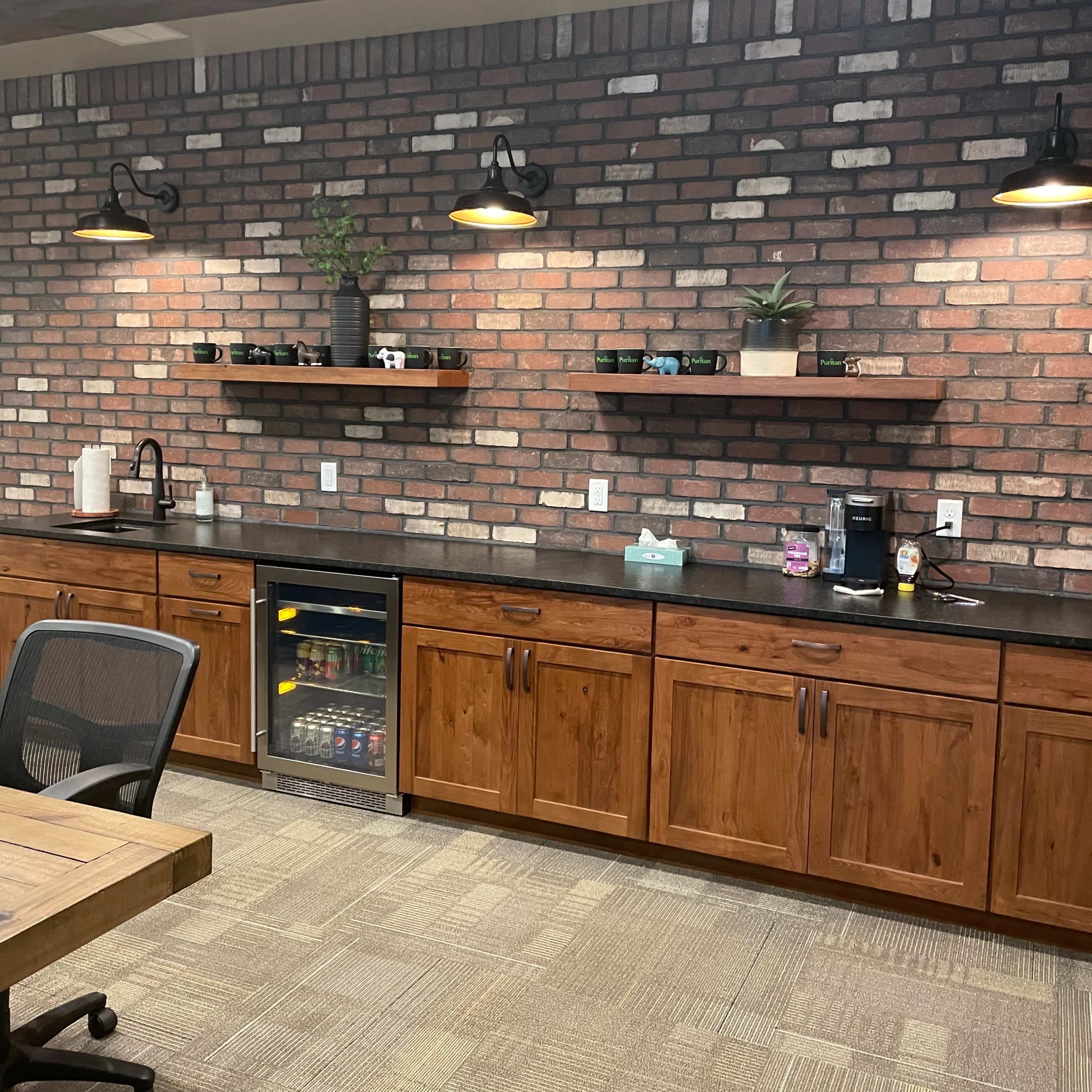 A modern kitchen with a brick wall, wooden cabinetry, open shelves displaying plants and decor, and a small wine cooler.
