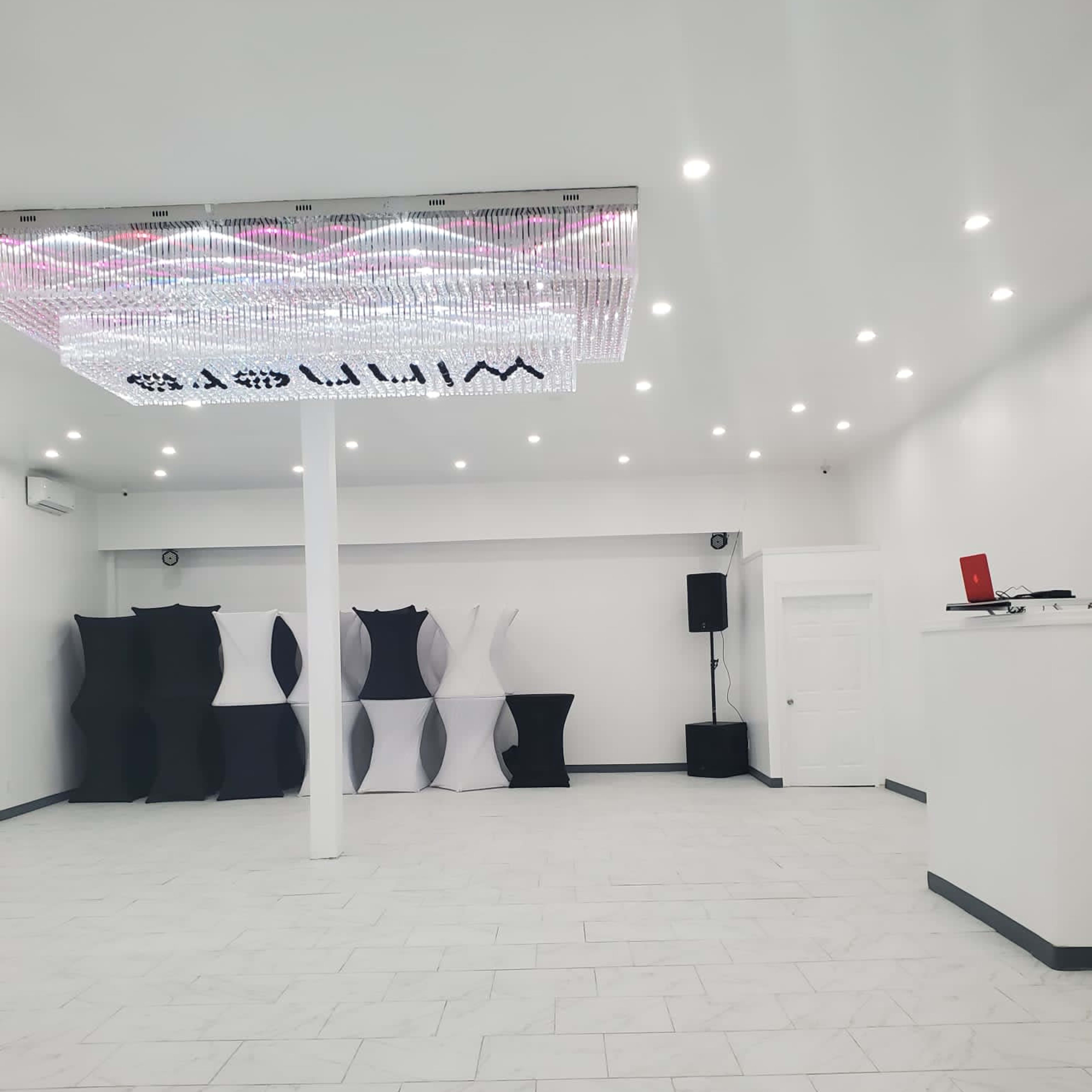 The interior of a spacious, modern room features a chandelier, white walls, and black and white display structures.