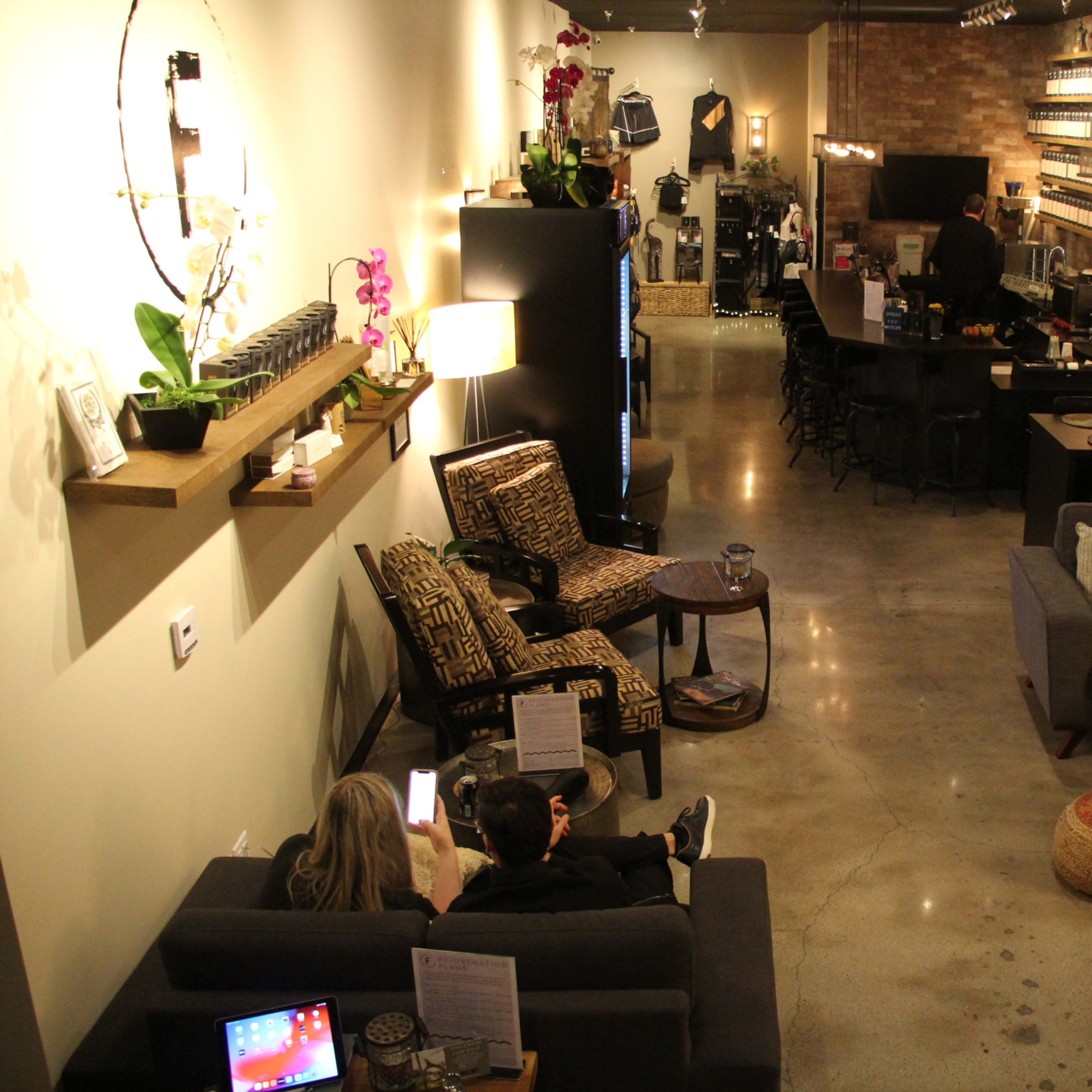 A stylish café interior with various seating arrangements, including sofas and chairs, along with decorative shelves and a bar area in the background.