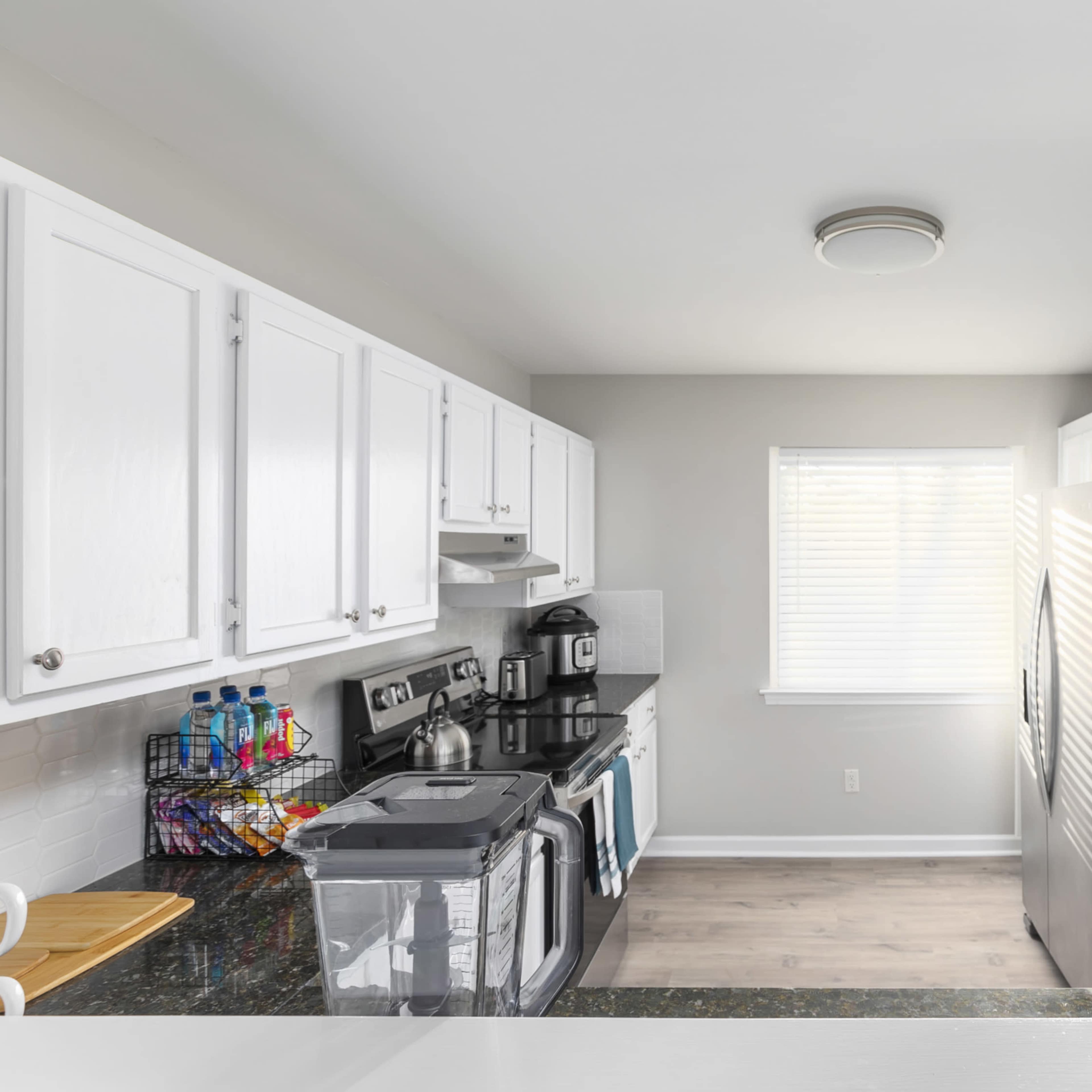 A modern kitchen features white cabinets, stainless steel appliances, and a window allowing natural light.