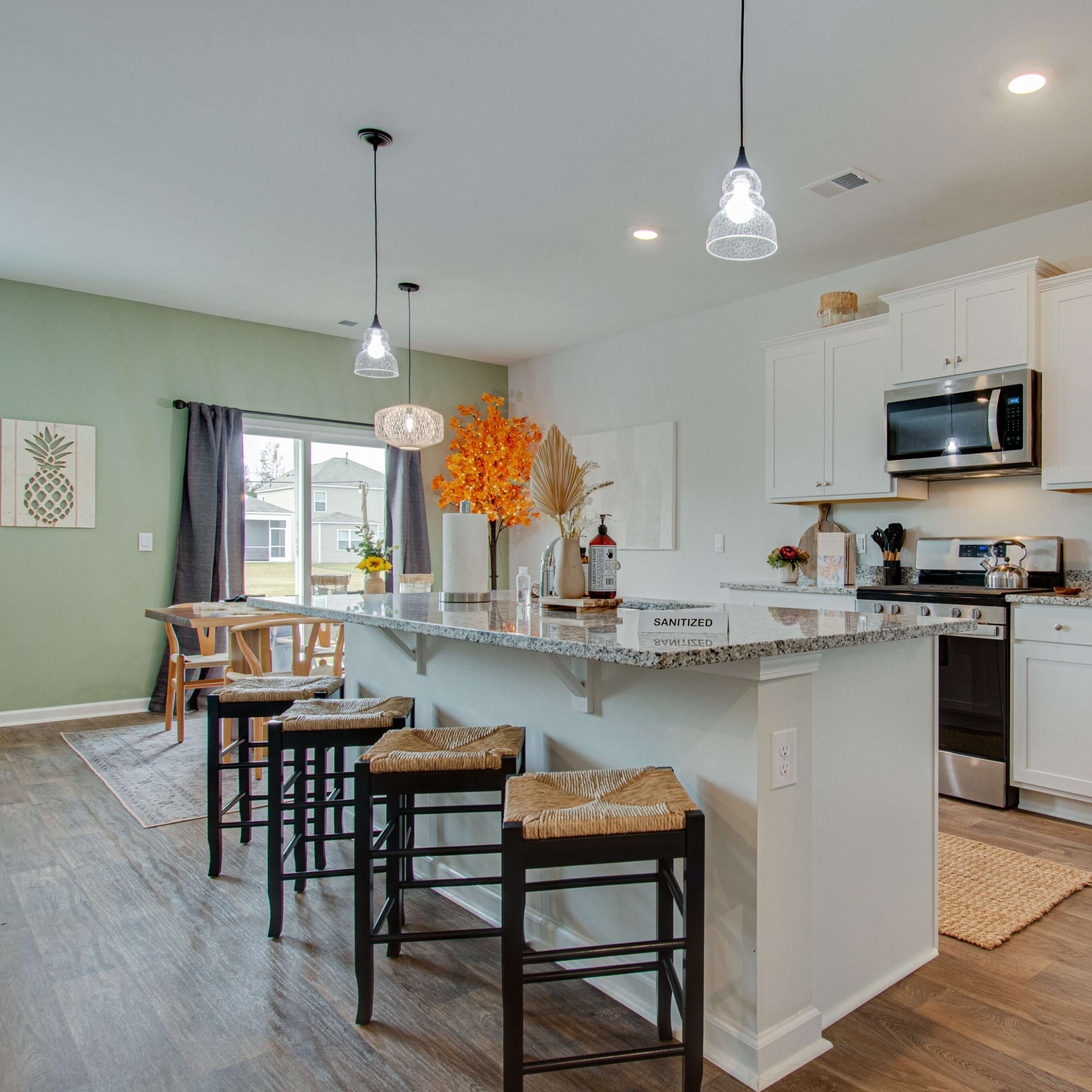 A modern kitchen with white cabinets, stainless steel appliances, a granite island, and bar stools, featuring a cozy dining area with natural light.