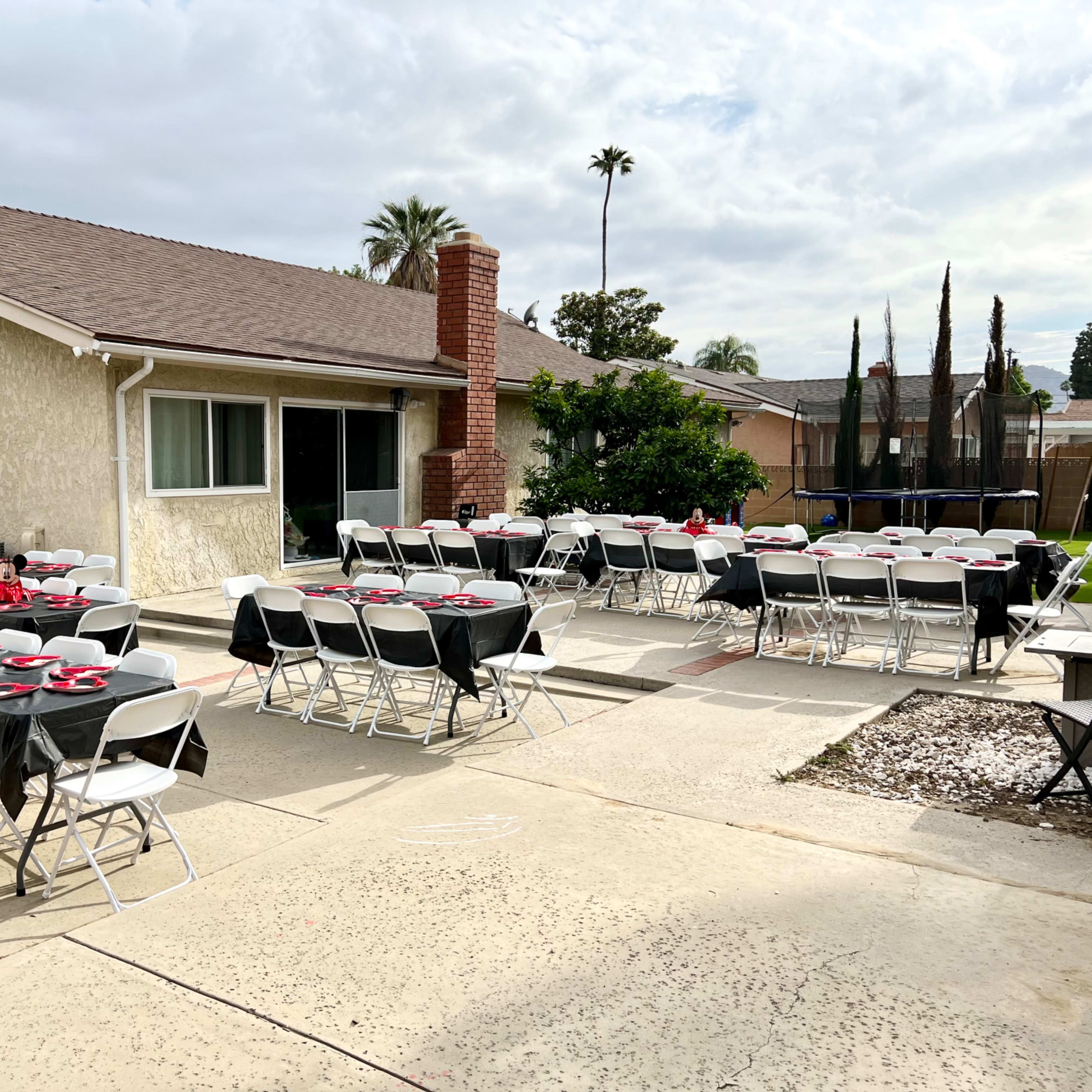 A patio is set up for an outdoor event with several tables covered in black tablecloths and red decorations.