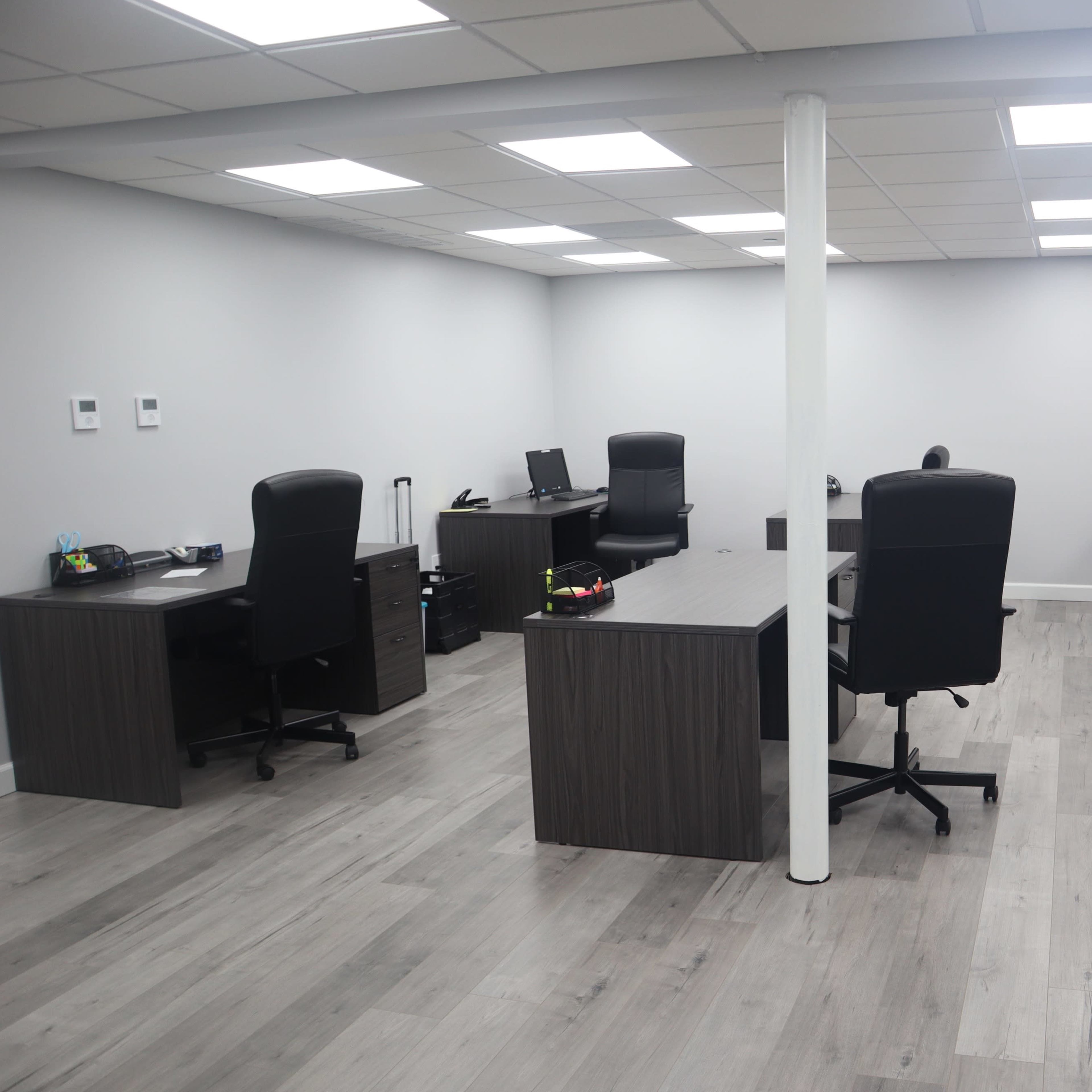 A modern office space with several desks and office chairs arranged in a minimalist layout under fluorescent lighting.