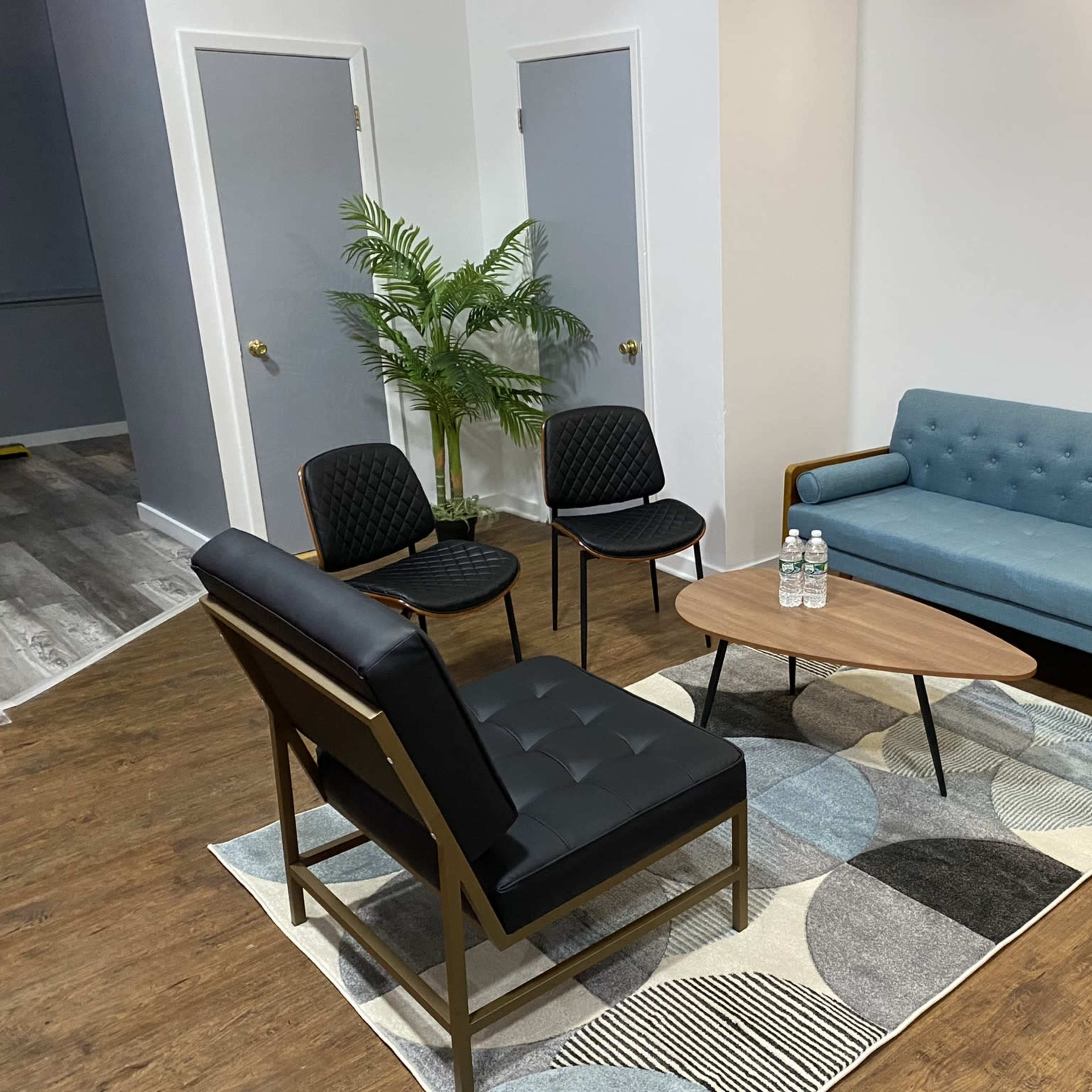 A small, modern seating area with a blue couch, four black chairs, a coffee table, and a patterned rug.