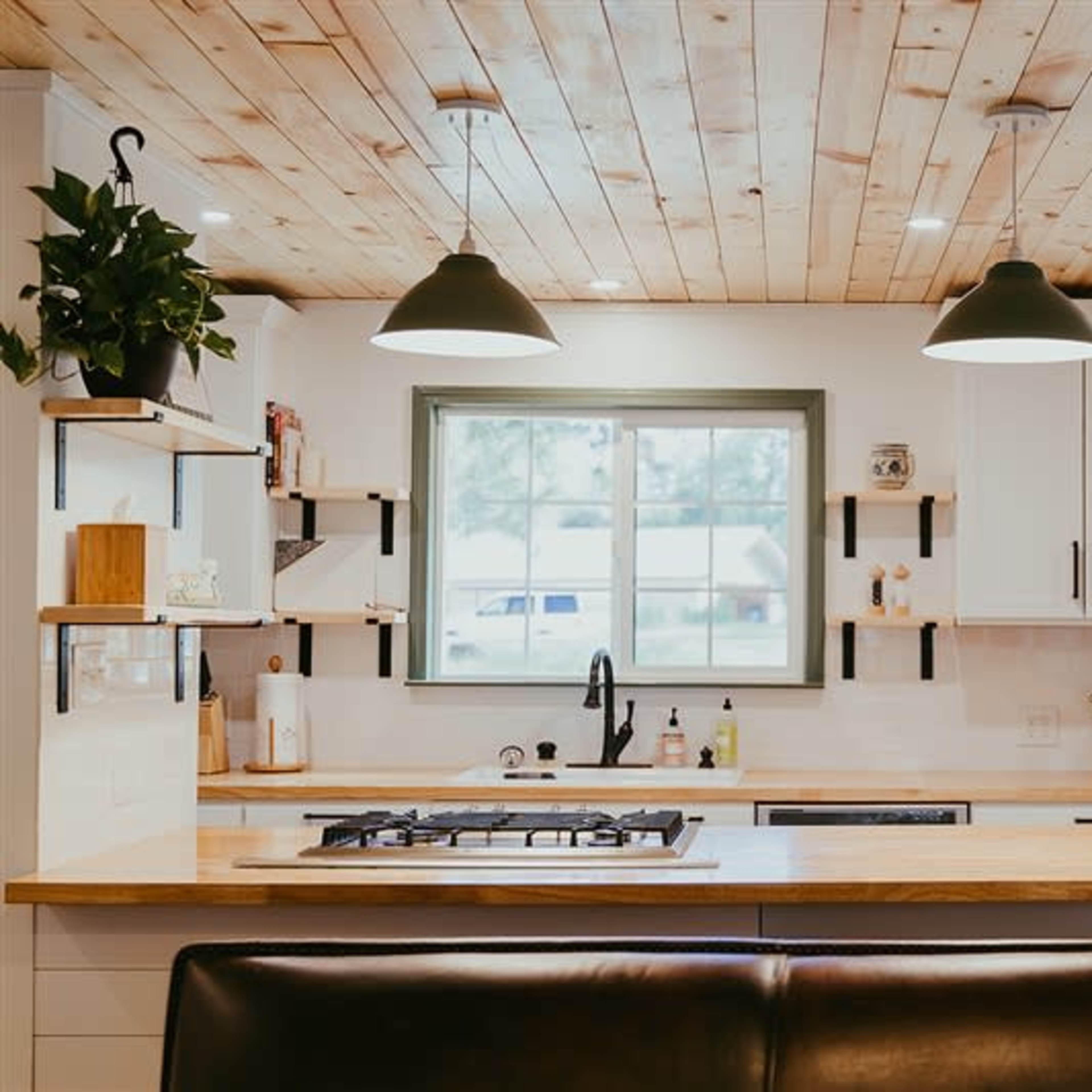 A modern kitchen features a central island with a gas stove, white cabinetry, and a large window above the sink.