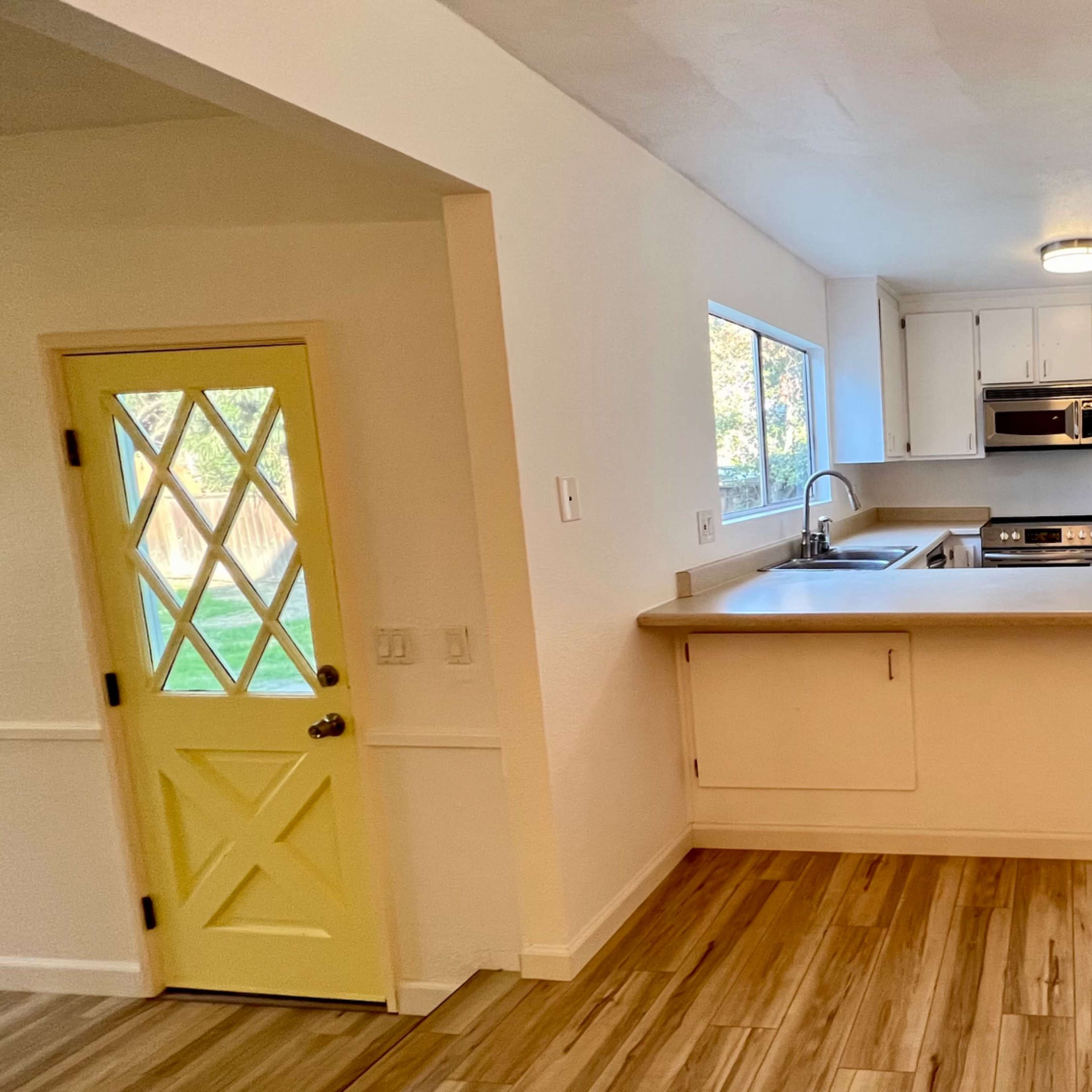 A modern kitchen with a light-colored countertop, white cabinets, and a window overlooking a backyard.