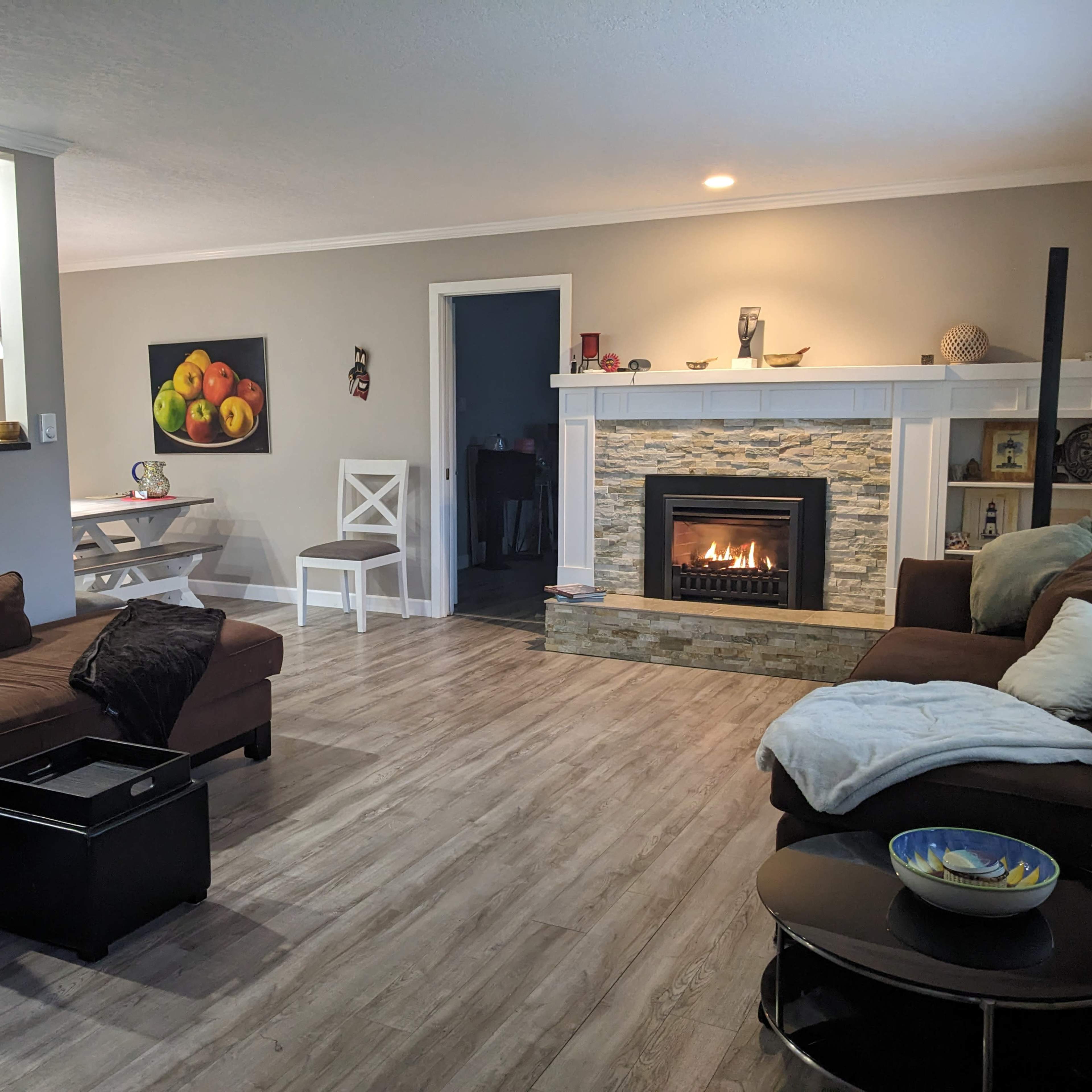 A cozy living room with a stone fireplace, two couches, a small coffee table, and a dining area in the background.