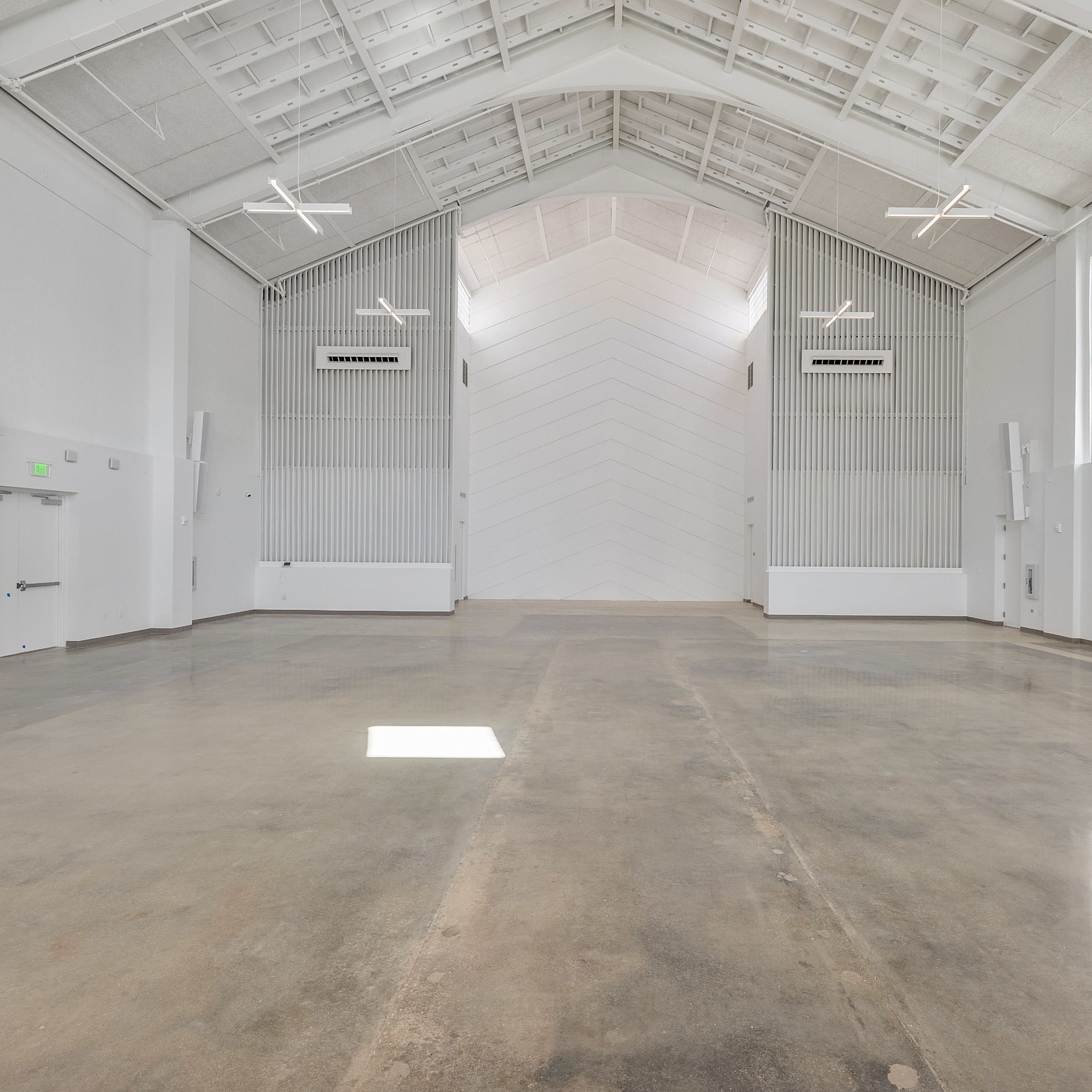 A spacious, empty hall with a high ceiling, large windows, and polished concrete flooring.